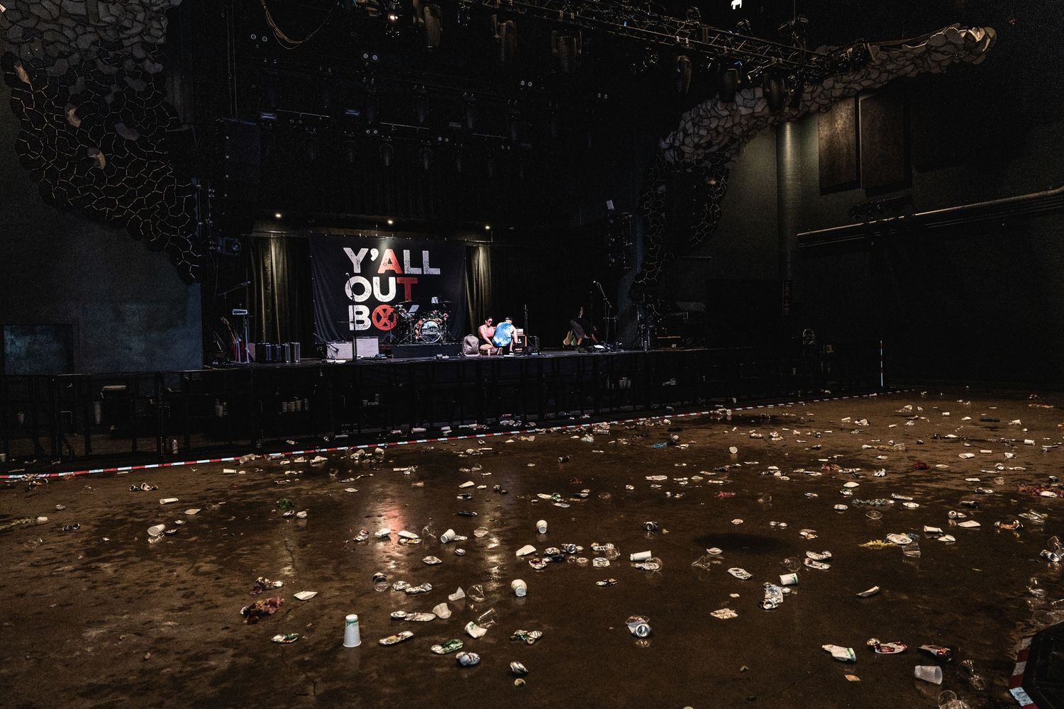 Empty concert venue after show with scattered debris on floor and distant lit stage.