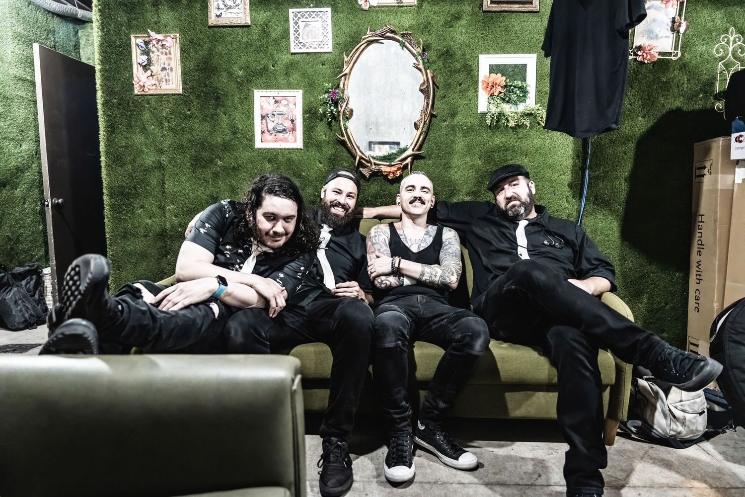 A group relaxes together on a green velvet couch with decorative frames and a mirror on the wall behind them.