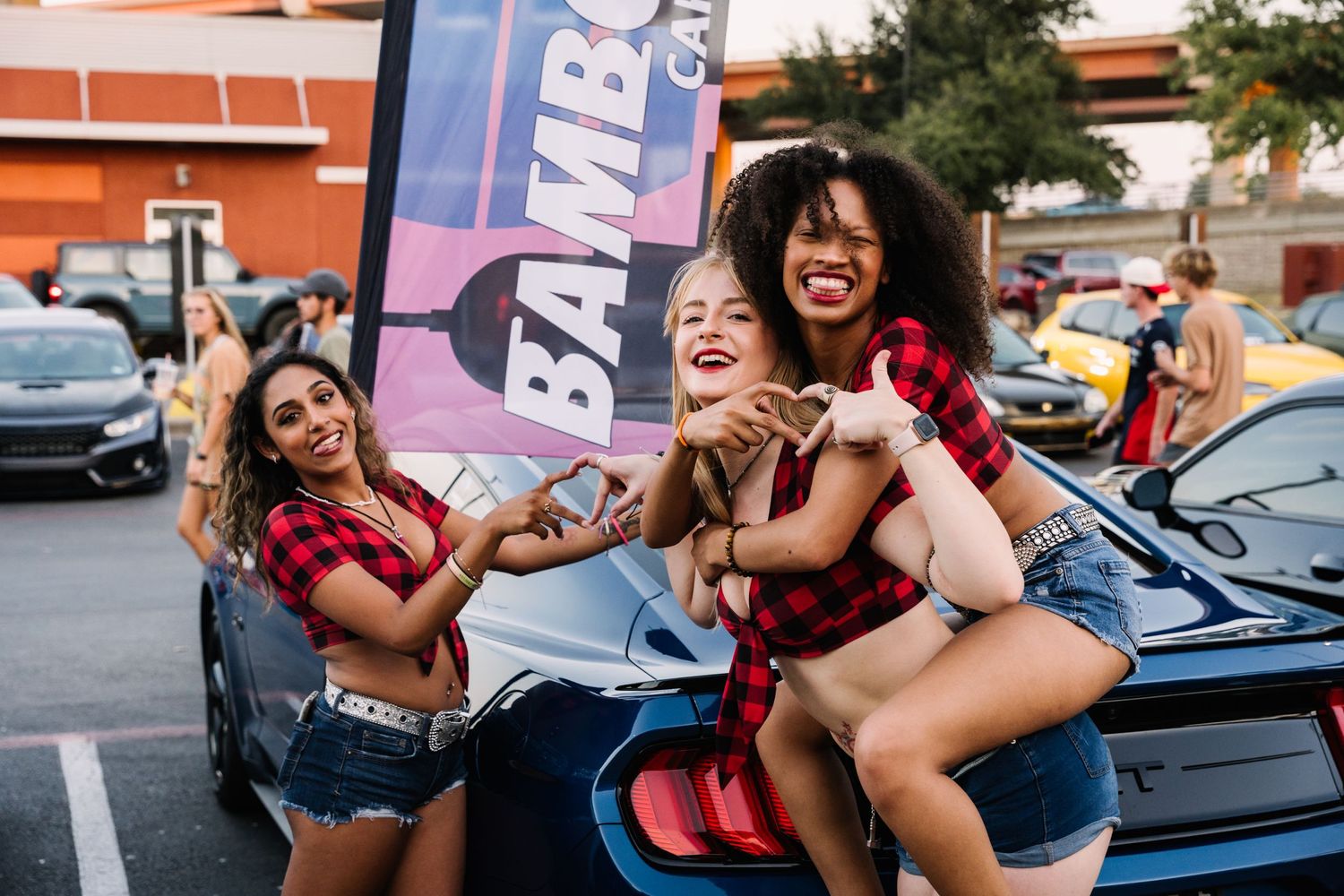 Friends having fun and posing together at a car meet in a parking lot.