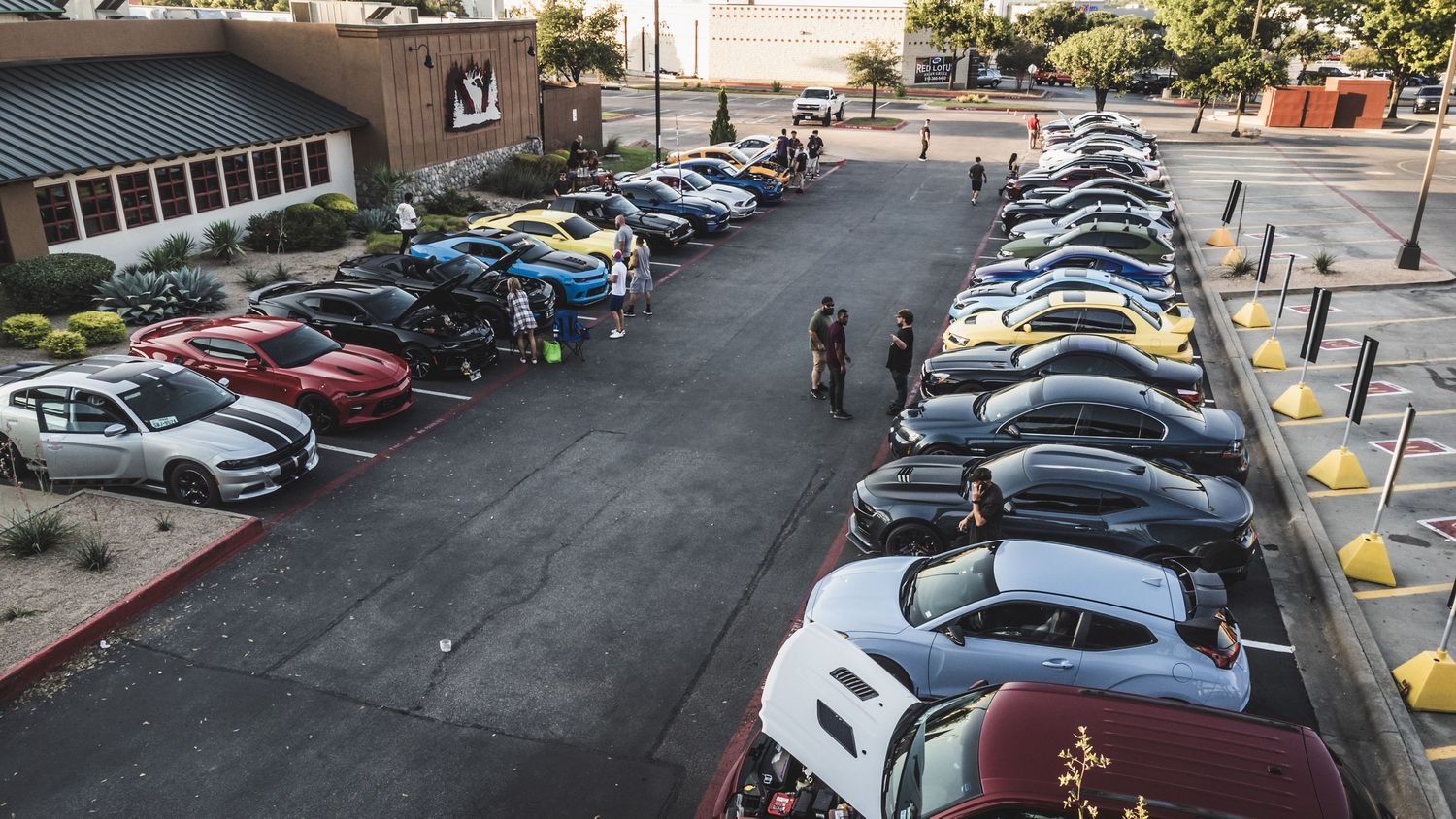 Overhead shot of car meet showing long rows of parked vehicles in parking lot.