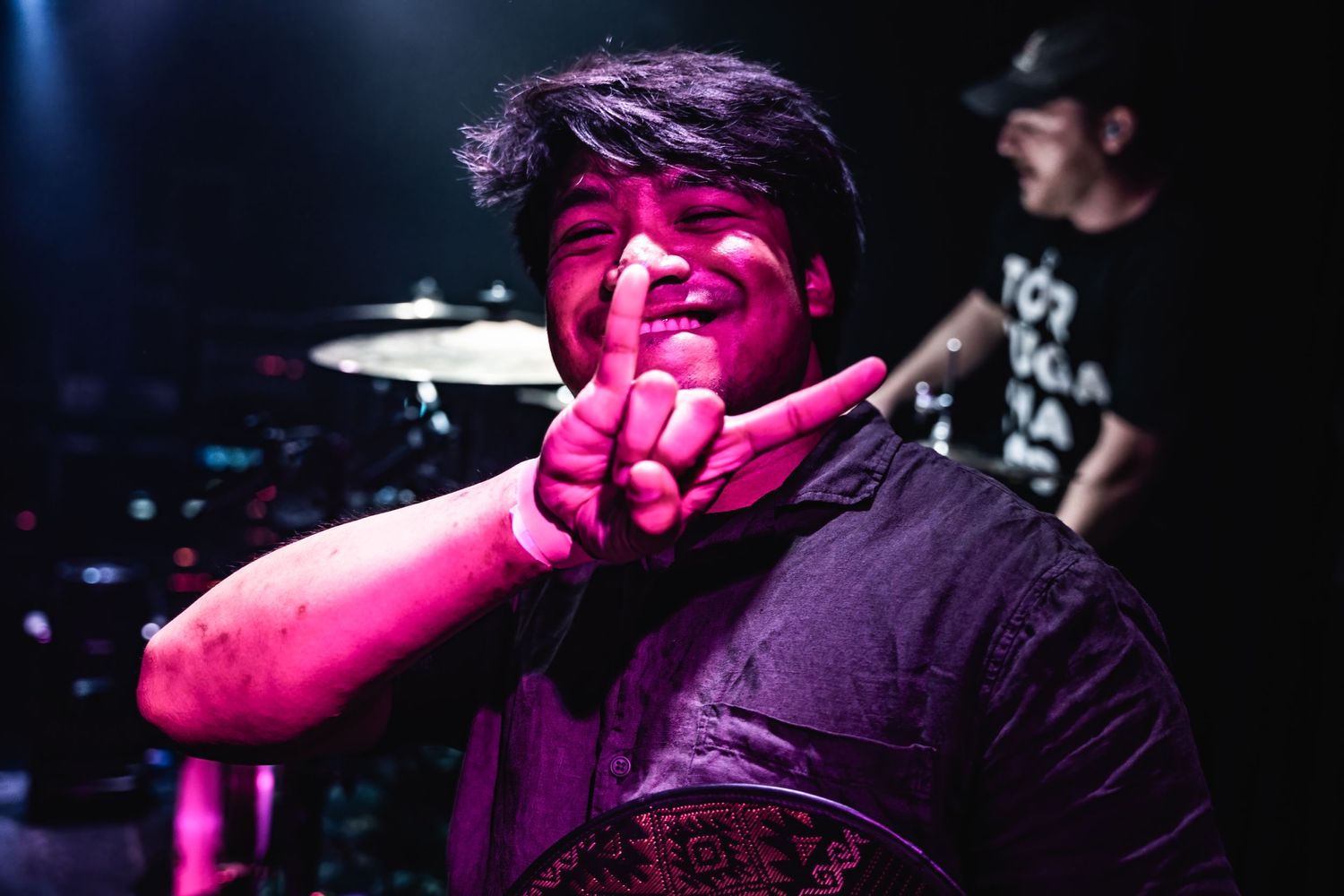 Performer makes hand gesture under vibrant pink stage lighting during live show.