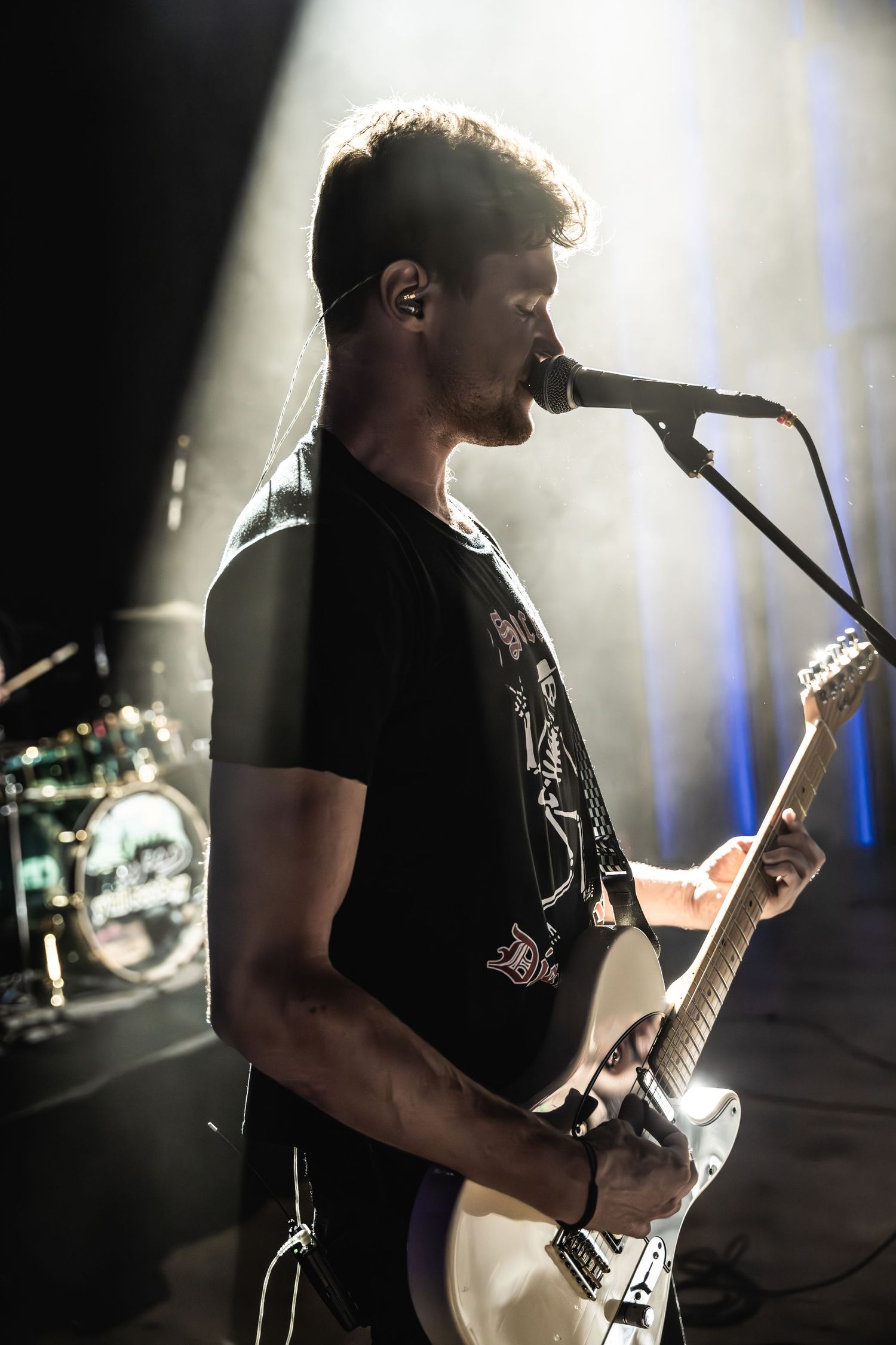 Silhouetted musician playing guitar and singing into microphone on dimly lit stage.
