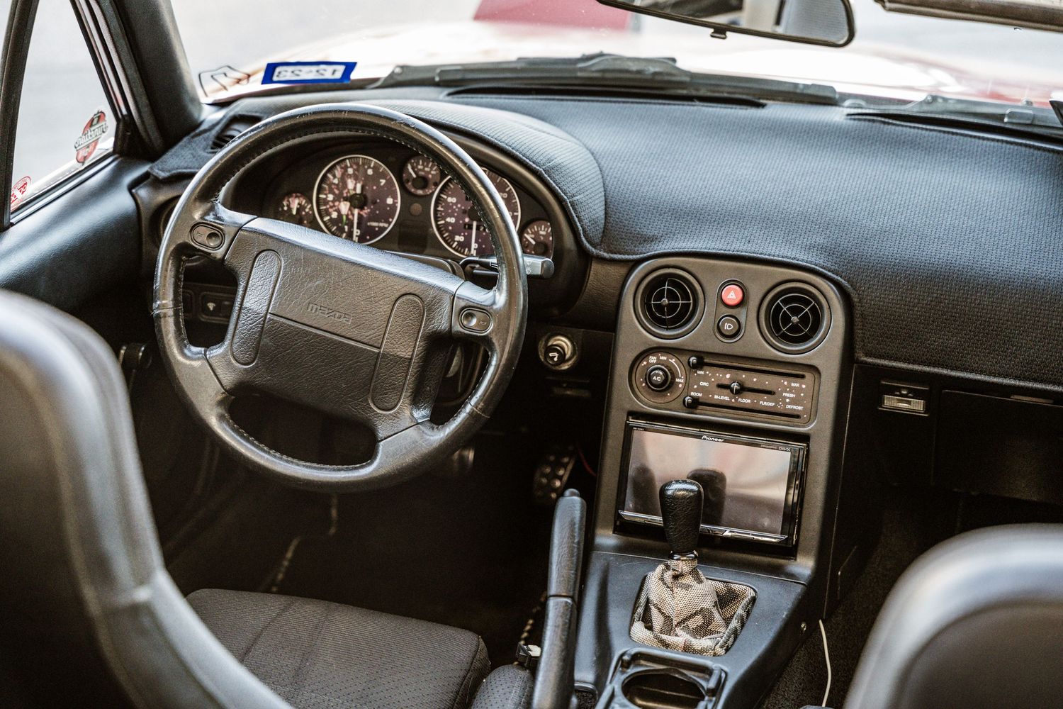 Classic car interior dashboard showing steering wheel and gauge cluster with carbon fiber trim.