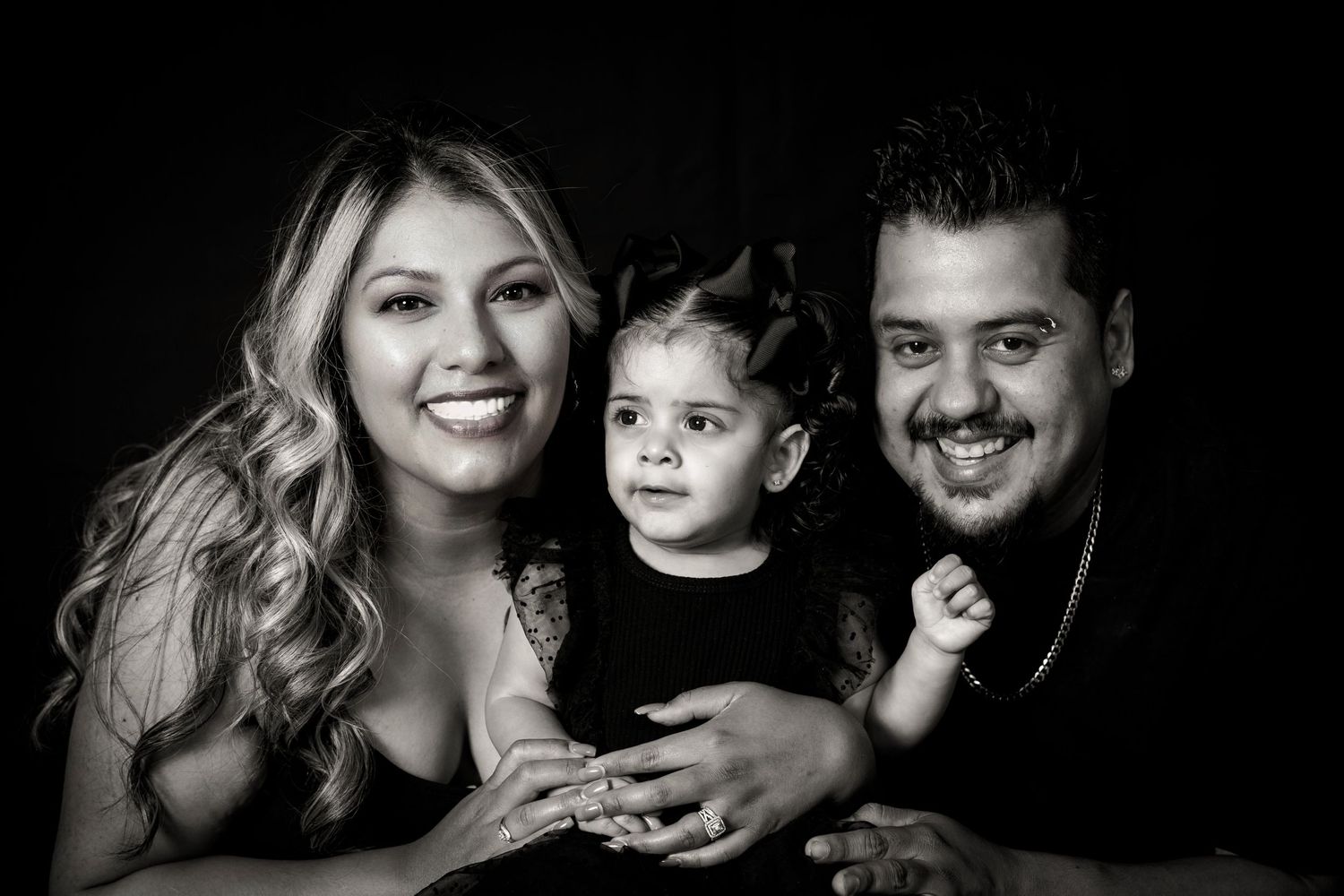 Classic black and white family portrait with child centered between parents against dark backdrop.