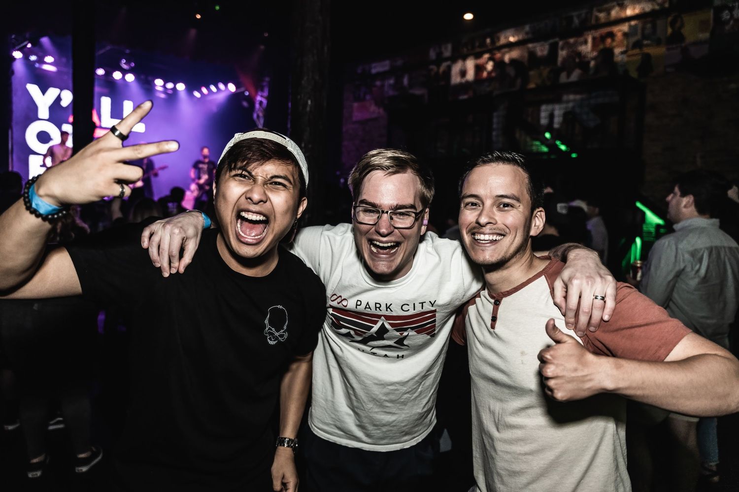 Friends celebrating and posing together at music venue with colorful stage lights in background.