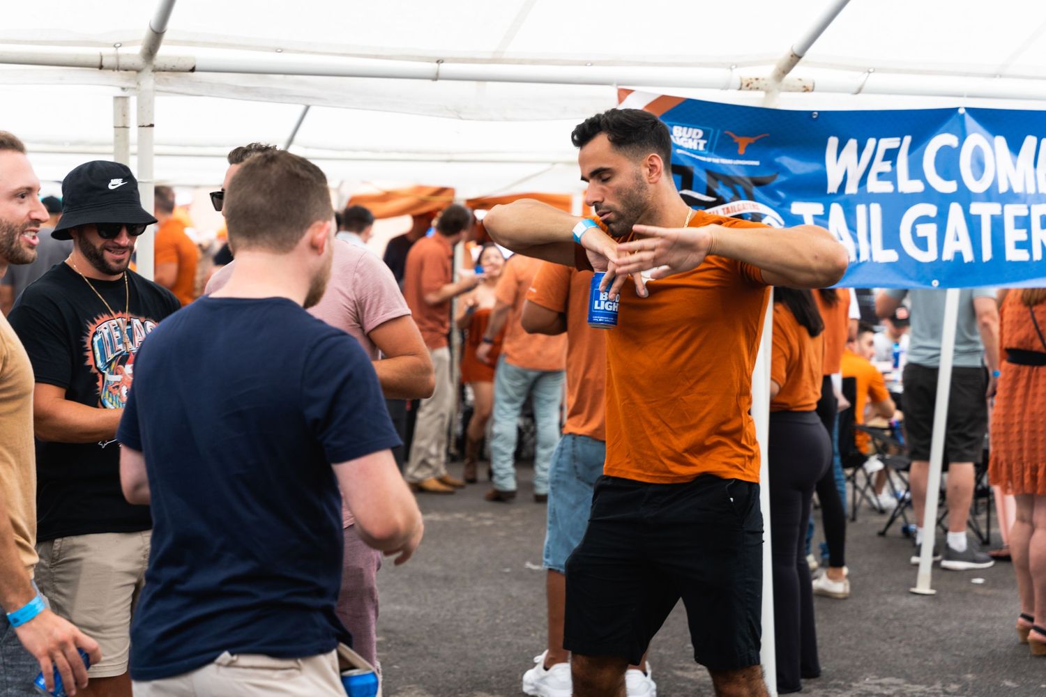 People socializing at a tailgate party with a Welcome Tailgaters banner visible.