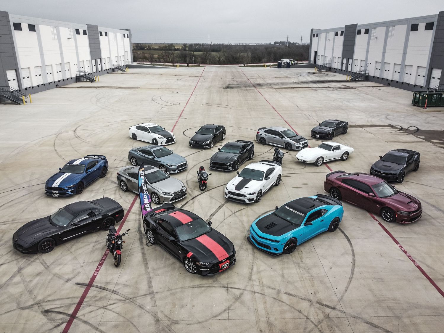 Collection of high-performance vehicles arranged in a curved formation on an industrial lot.