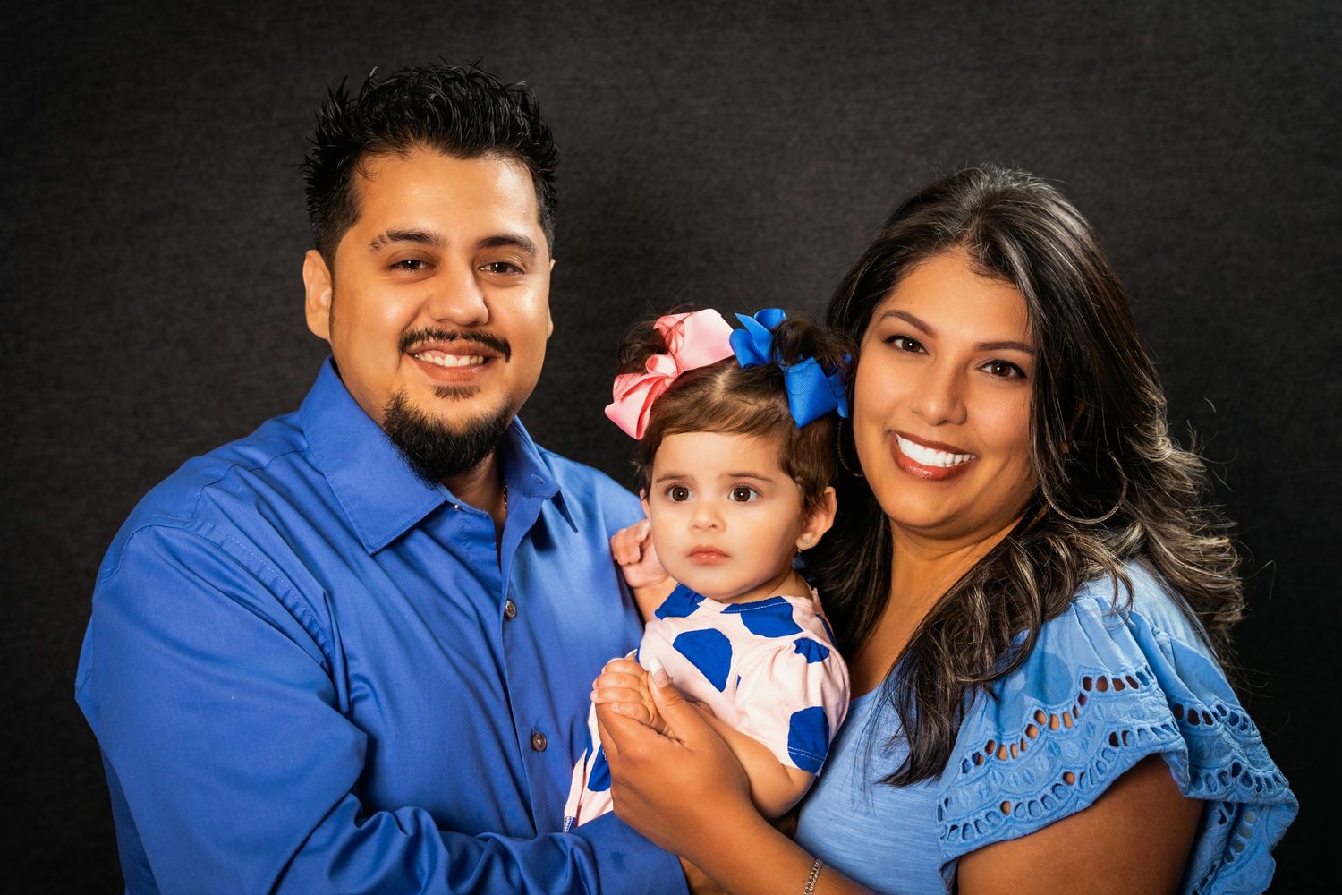 Studio family portrait showing joyful expressions as parents embrace their young daughter.