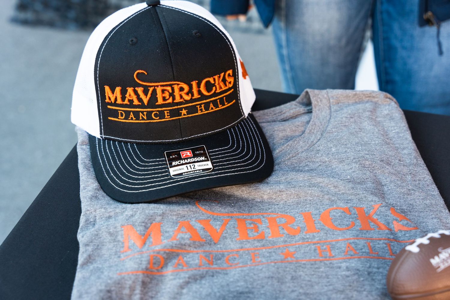 Close up of Mavericks Dance Hall merchandise including black baseball cap and gray t-shirt.