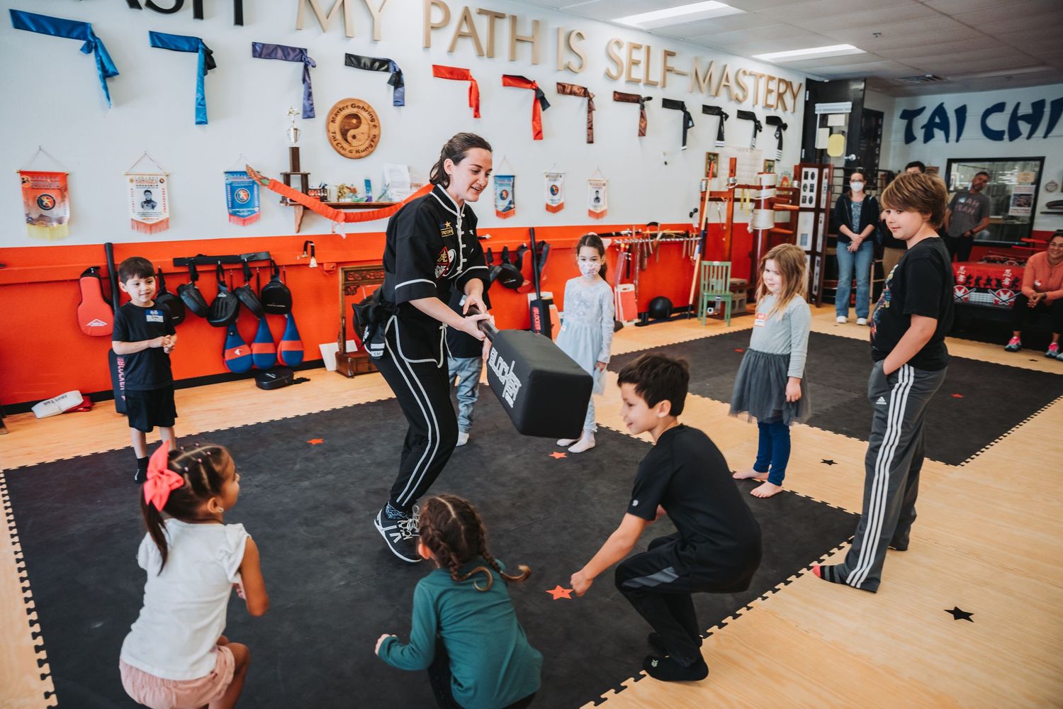 Group training session in a martial arts studio with decorative banners and equipment on walls.
