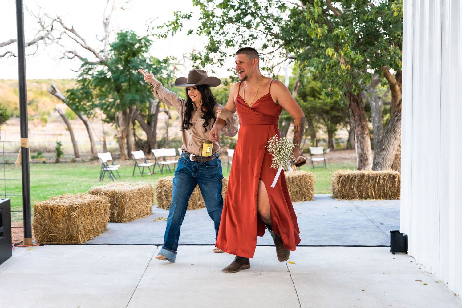 Two dancers perform in western-inspired outfits on outdoor dance floor with hay bales.