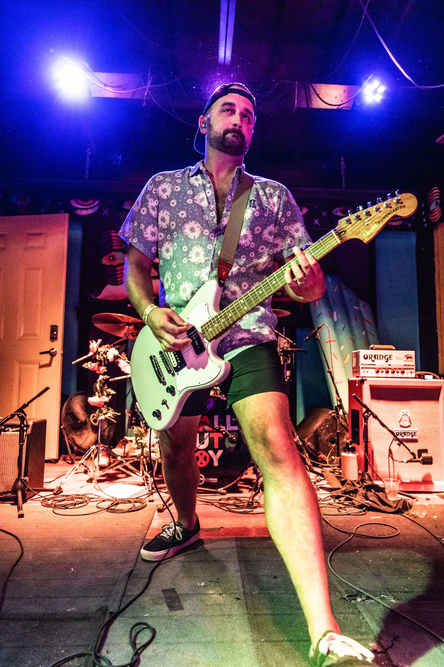 Musician playing mint green electric guitar on stage under purple lighting.