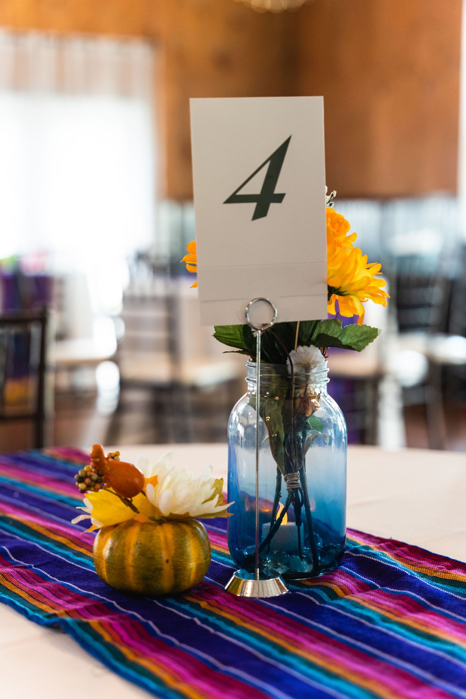 Table number 4 centerpiece with sunflower in blue mason jar and small pumpkin on striped runner.