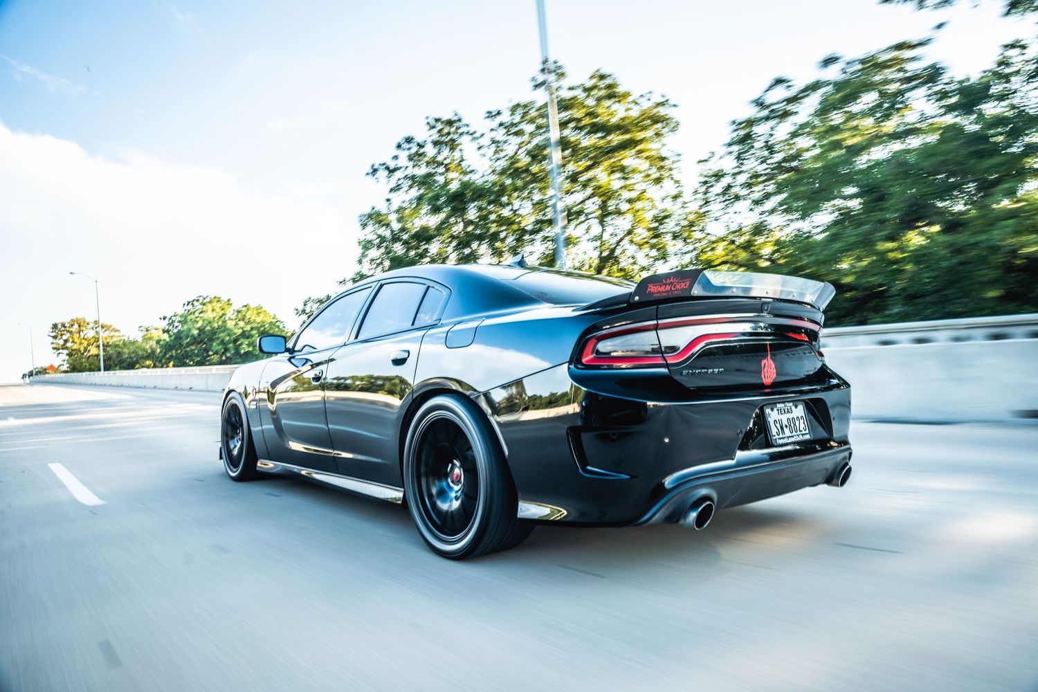 Black Dodge Charger with aftermarket wheels and body kit captured in dynamic rolling shot.