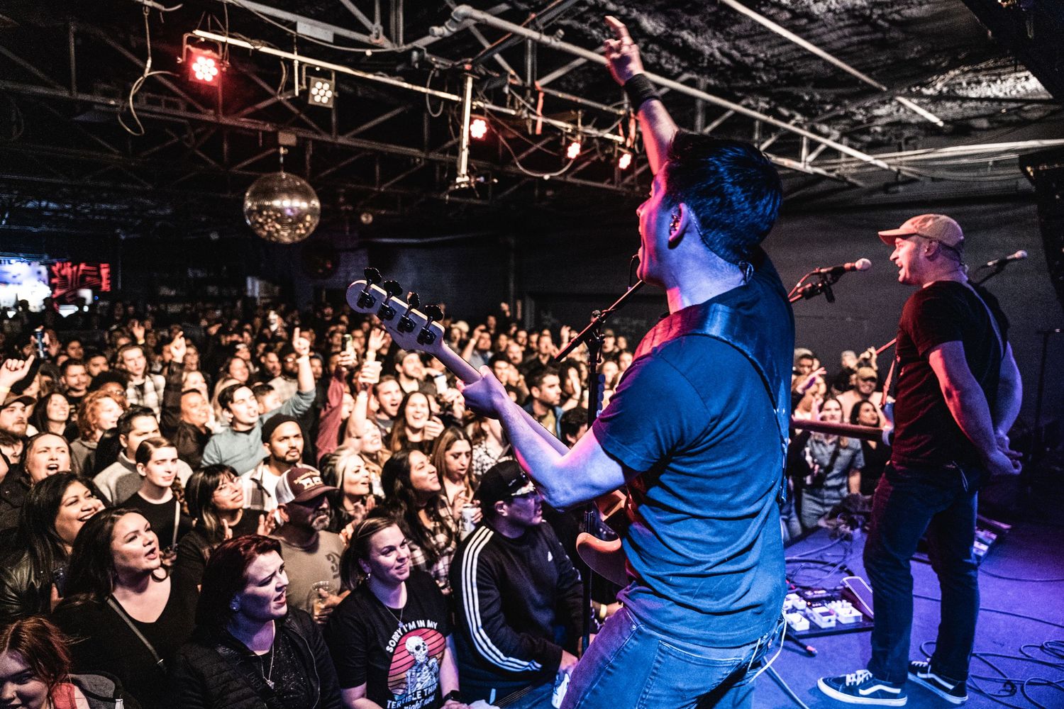 Energetic concert performance with band on stage and crowded audience in dark venue.