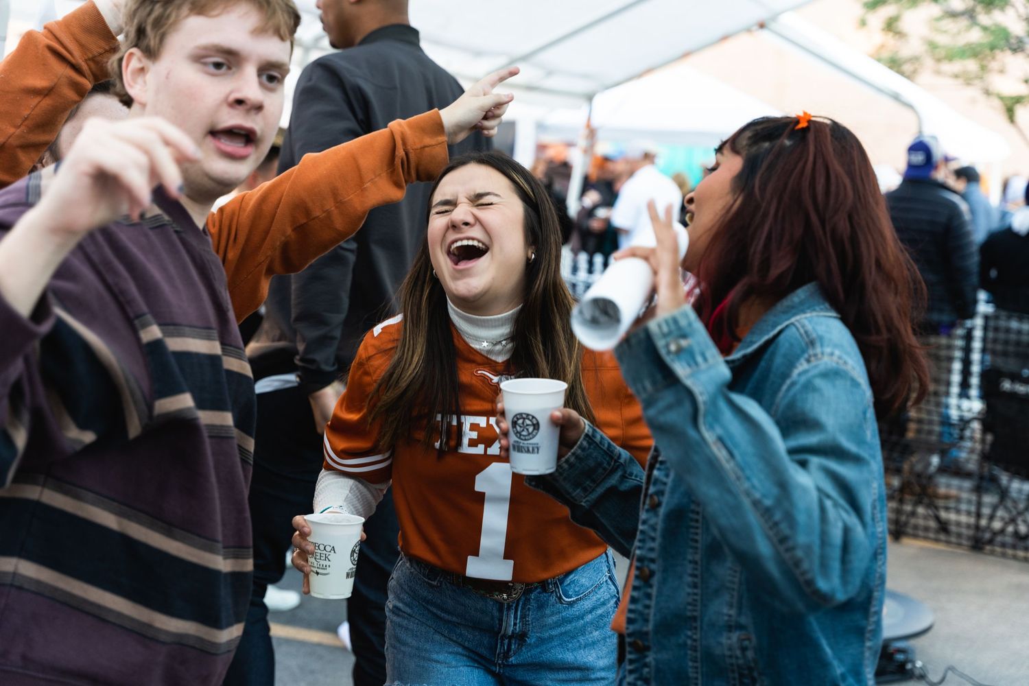 Friends enjoying a lively moment at an outdoor campus celebration wearing university apparel.