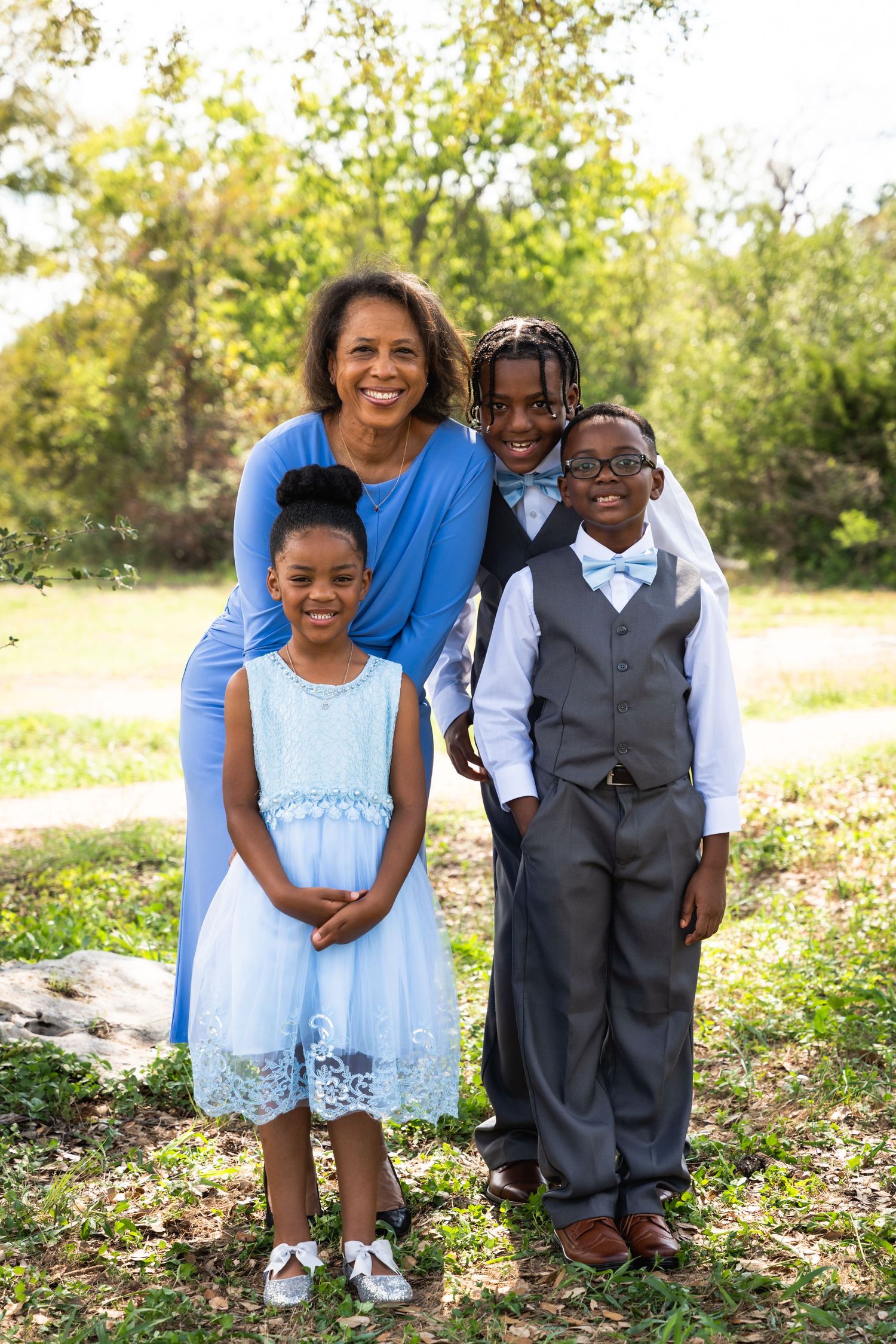 A family of four poses together outdoors on a sunny day wearing dressy attire.