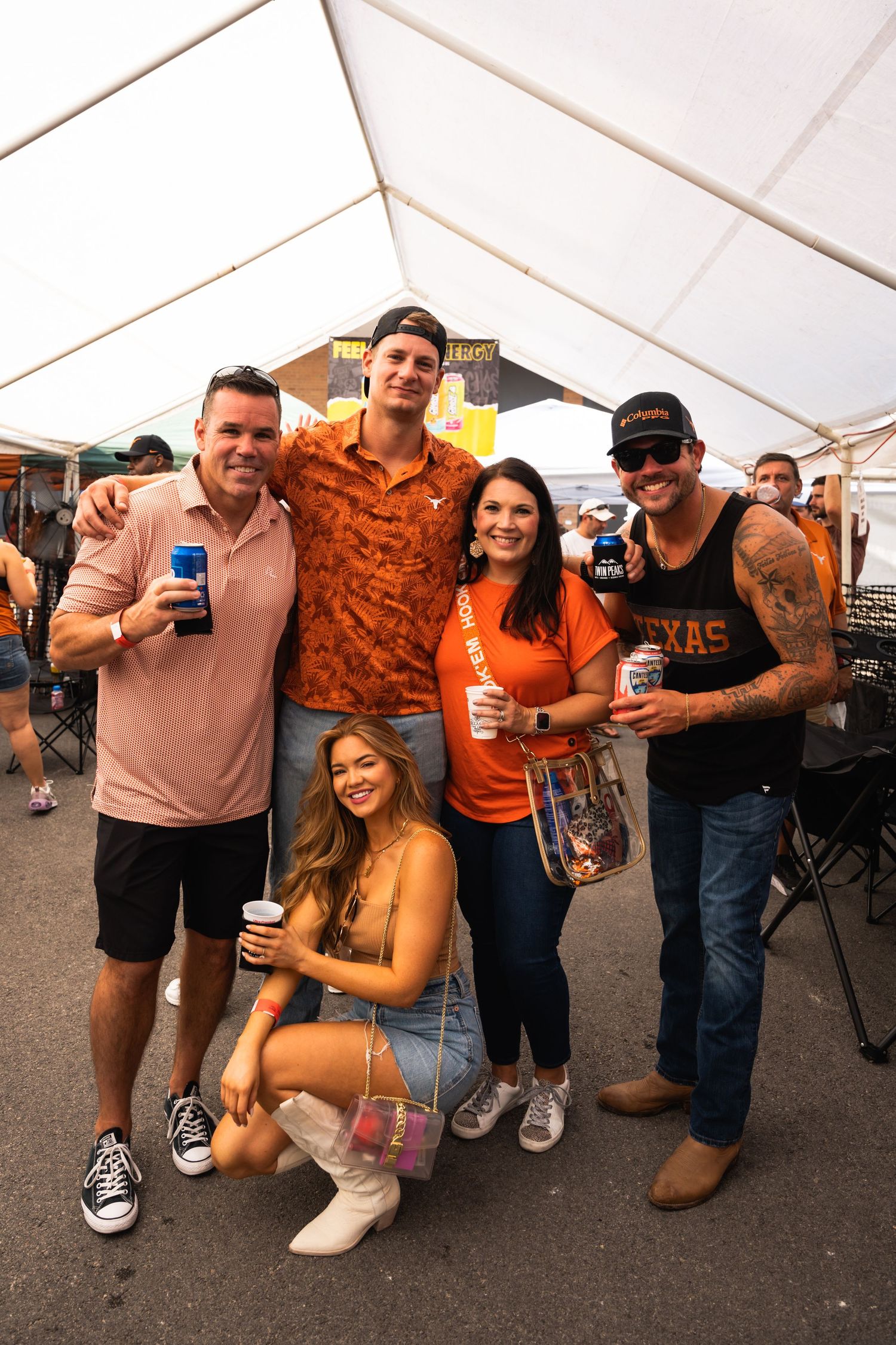 Group of friends pose together at a Texas tailgate event under a white tent.