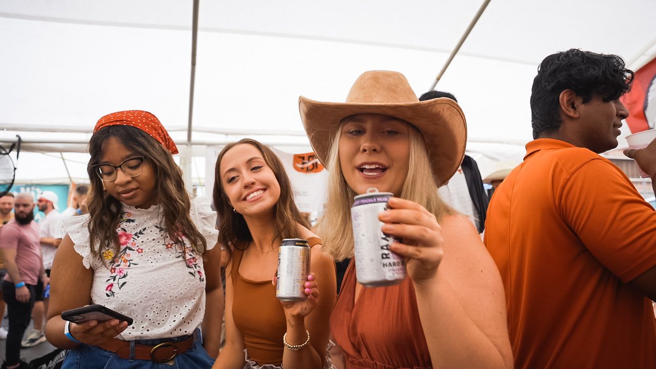 Festival-goers in cowboy hats and summer attire enjoying drinks at outdoor event.