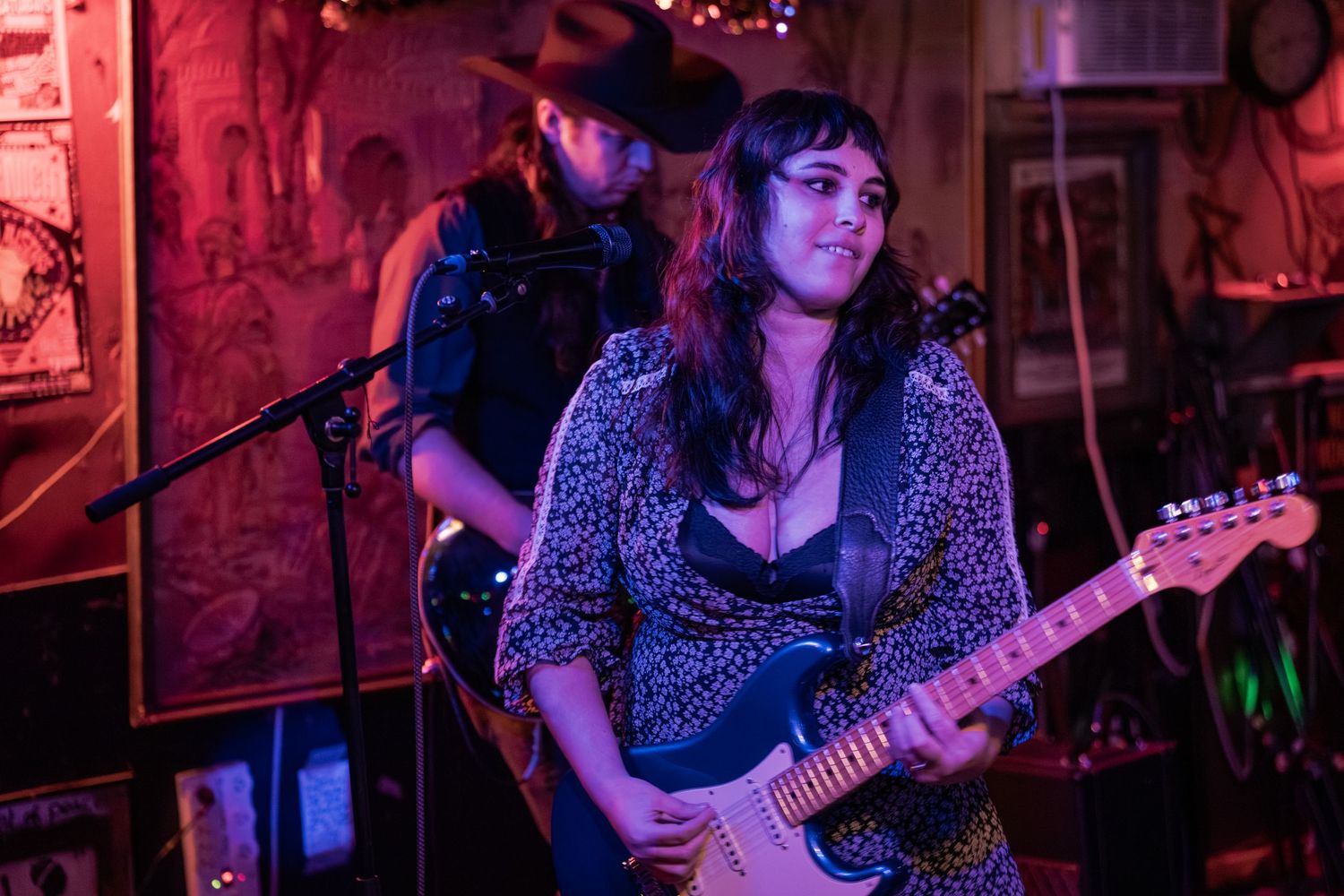 Bass player performs under purple stage lighting while wearing a polka dot dress at a live music venue.