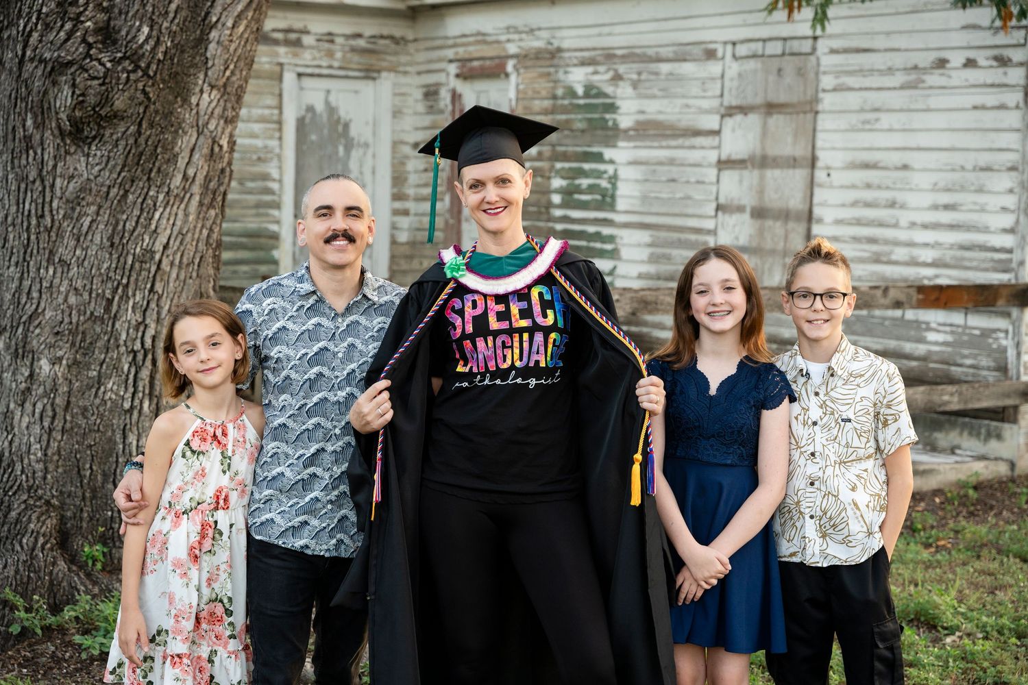 A graduation portrait of a group standing together against a rustic white wooden wall background.
