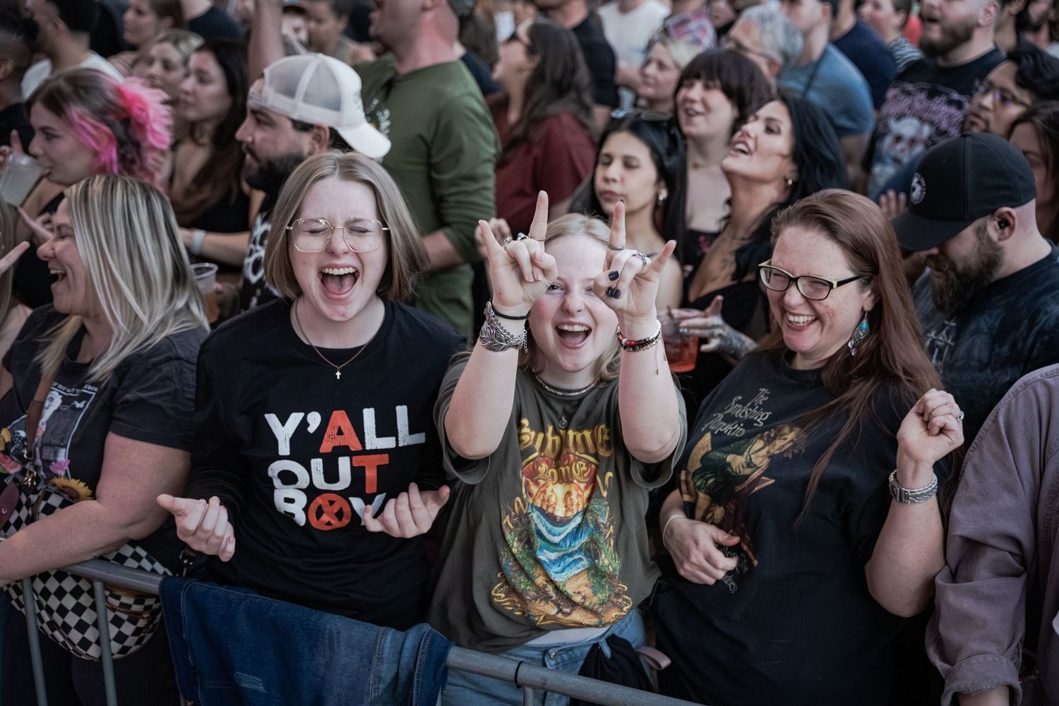 Excited concert fans cheering and making rock hand gestures at an outdoor music festival.