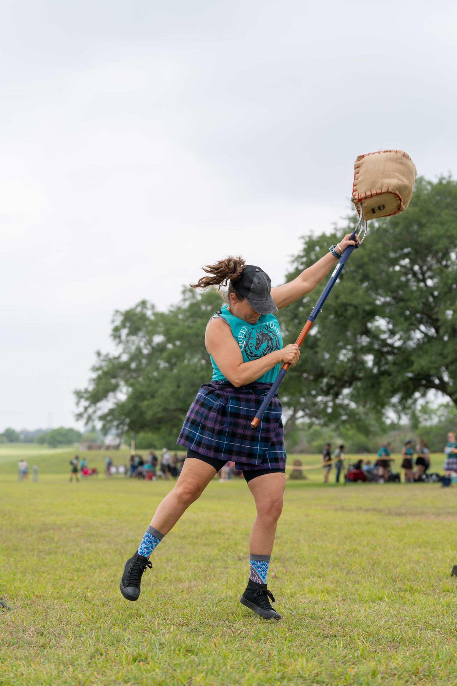 Woman in tartan kilt competes in Highland Games hammer throw on green field during outdoor athletic competition.