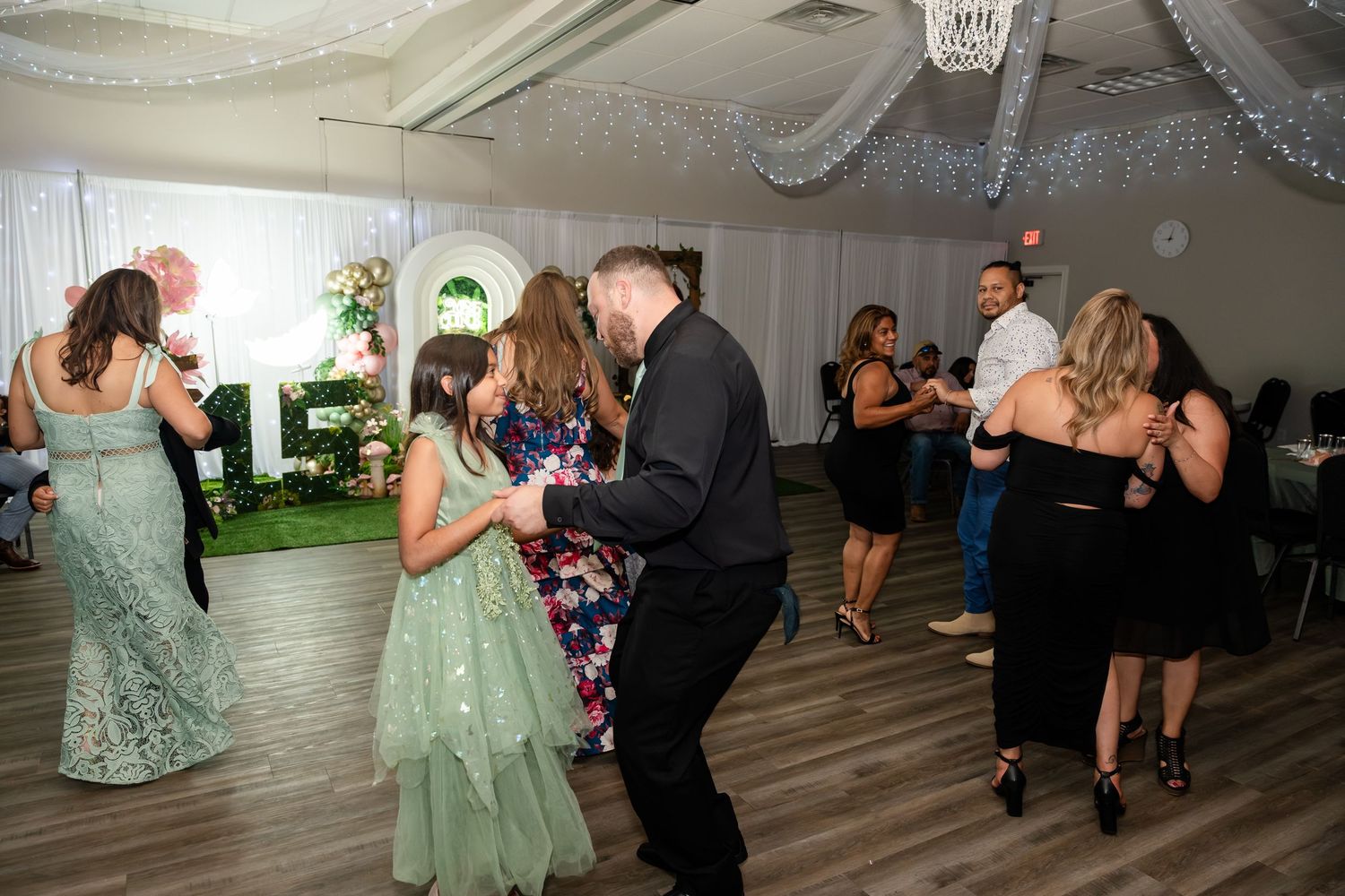 Guests dancing joyfully at an elegant wedding reception with white drapes and string lights.