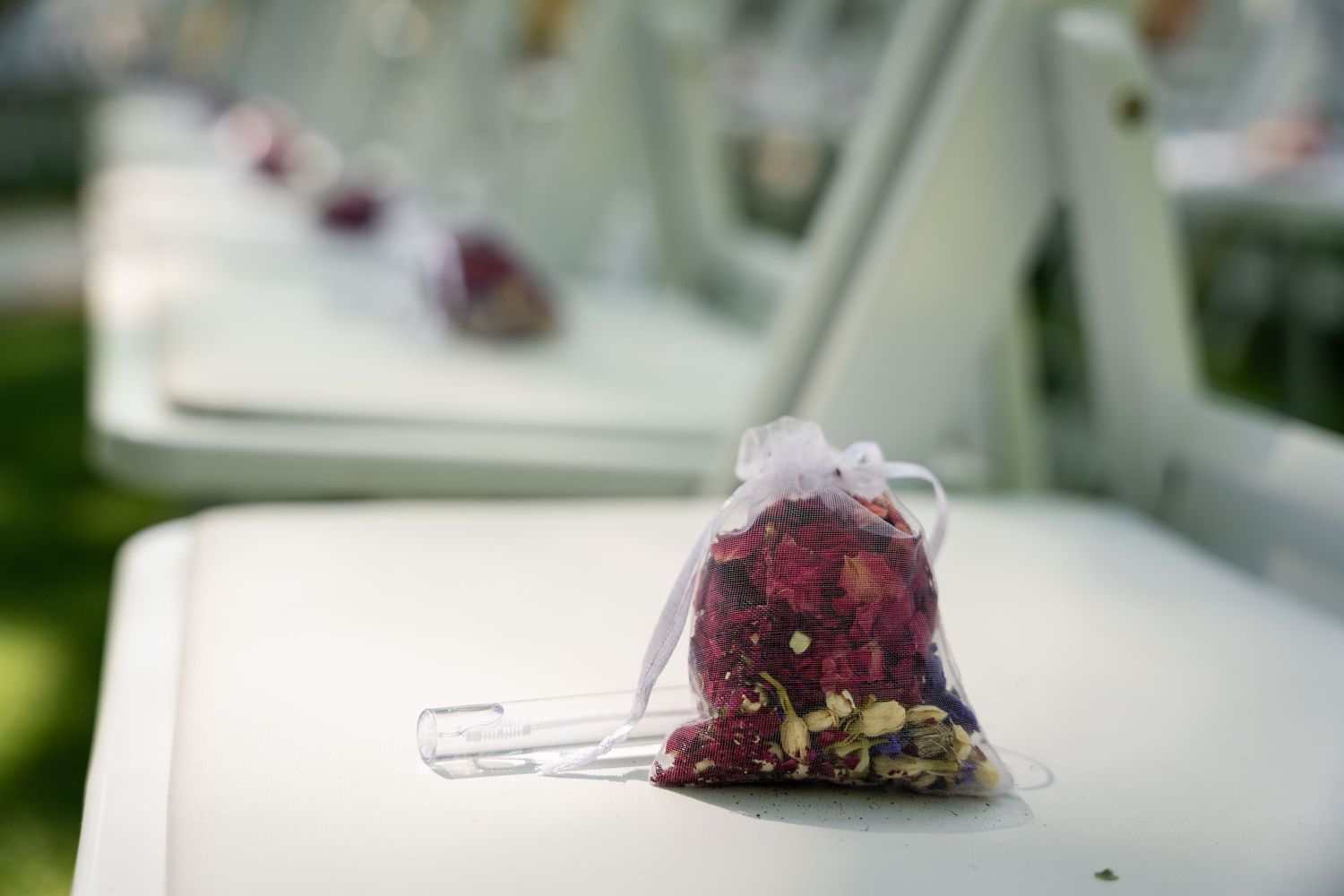 Small organza bags filled with colorful flower petals placed on white chairs at an outdoor wedding ceremony.
