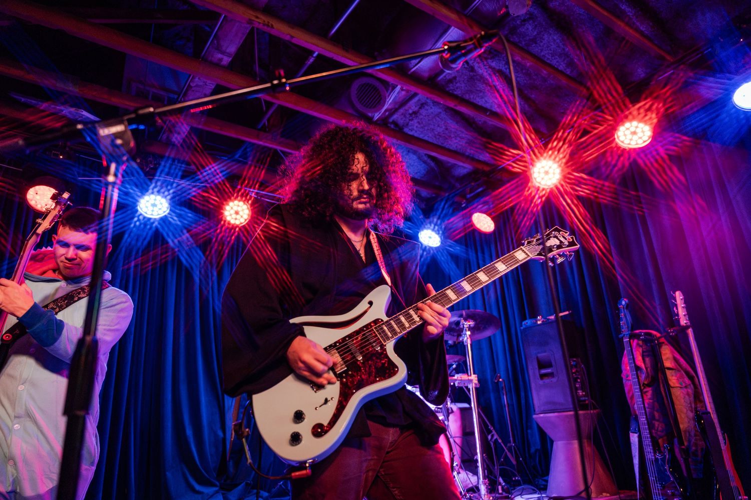 A rock band performs on stage with colorful blue and red lighting illuminating the concert venue.