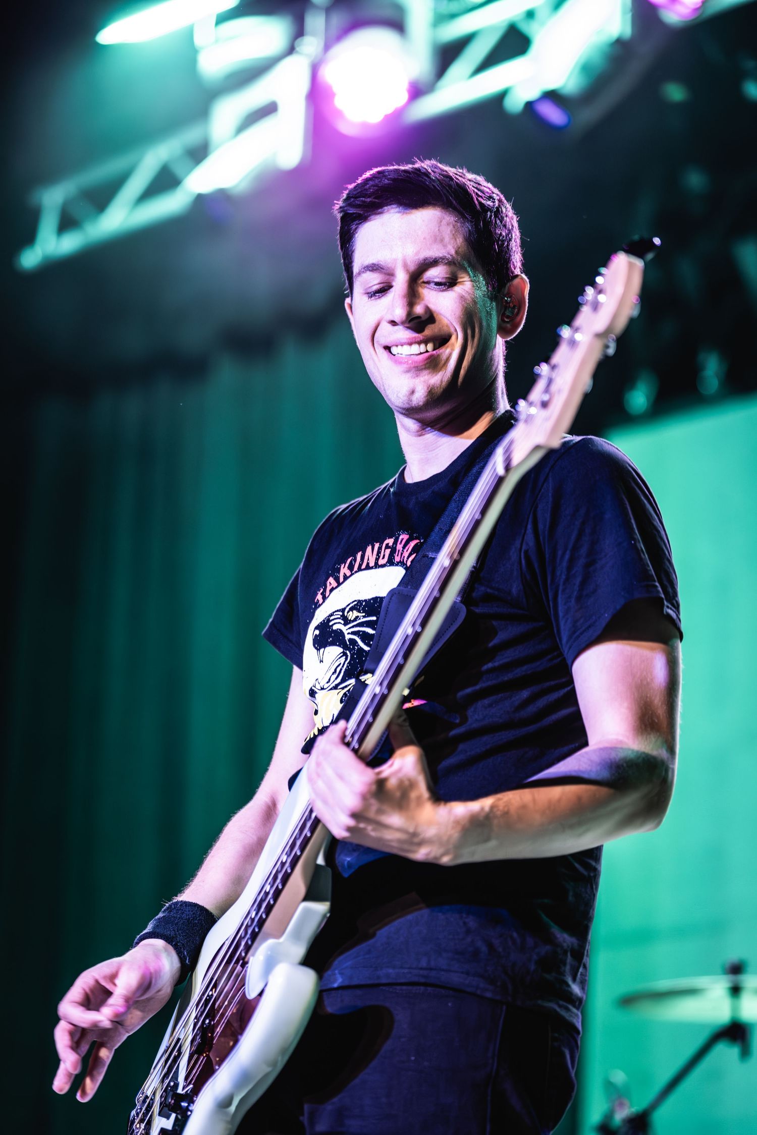 Musician plays bass guitar while smiling under colorful stage lights.