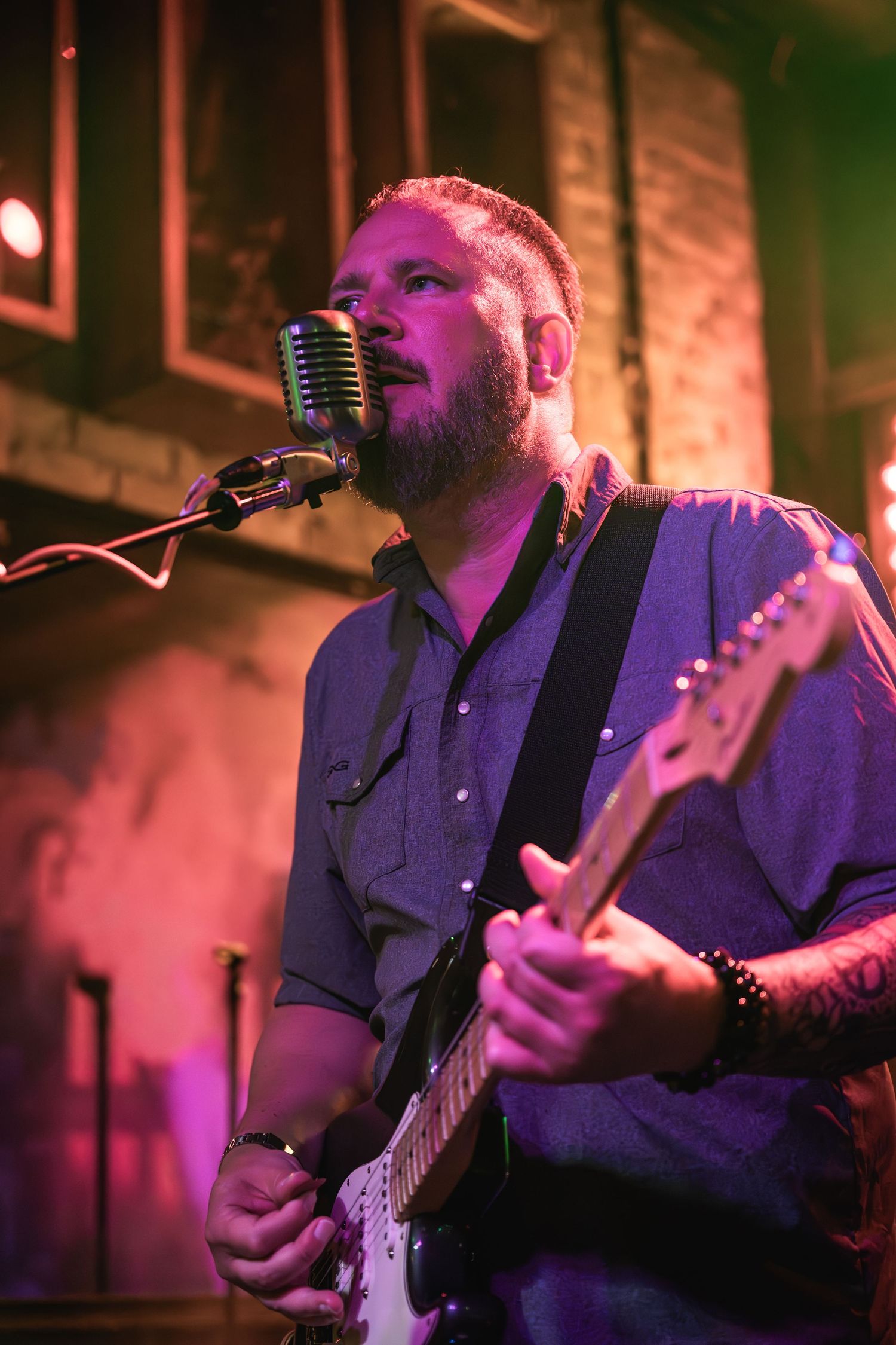 Musician performs with guitar and vintage microphone under purple stage lighting.