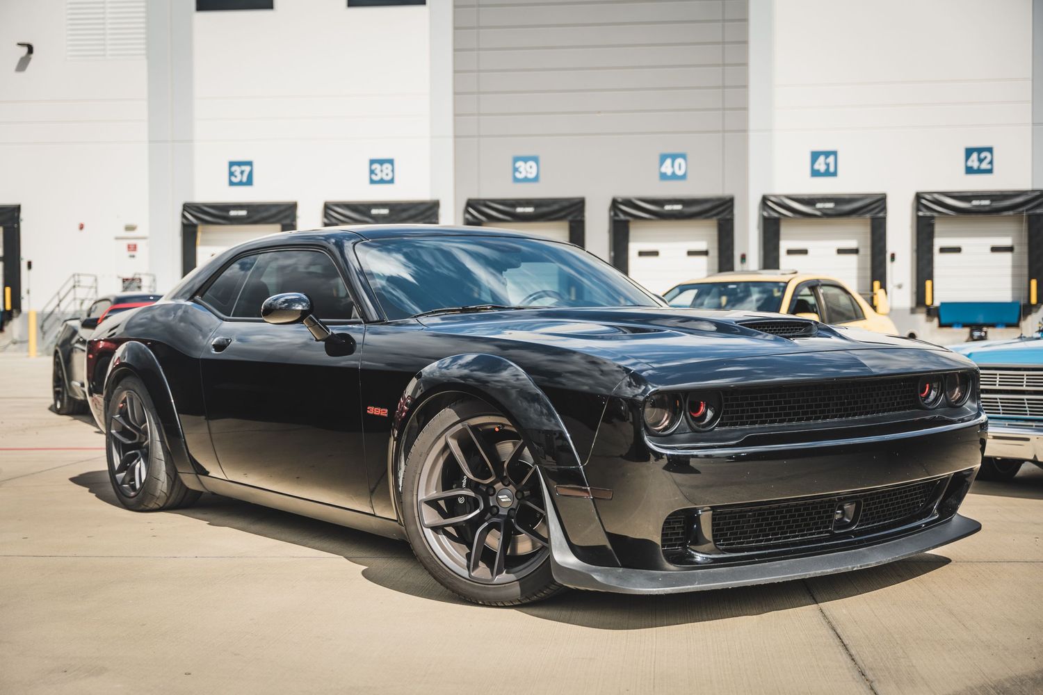 Black Dodge Challenger with custom wheels and wide body kit beside loading bay.
