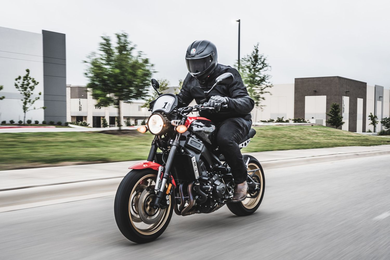 Sport bike rider leans into turn while cruising past modern commercial buildings.