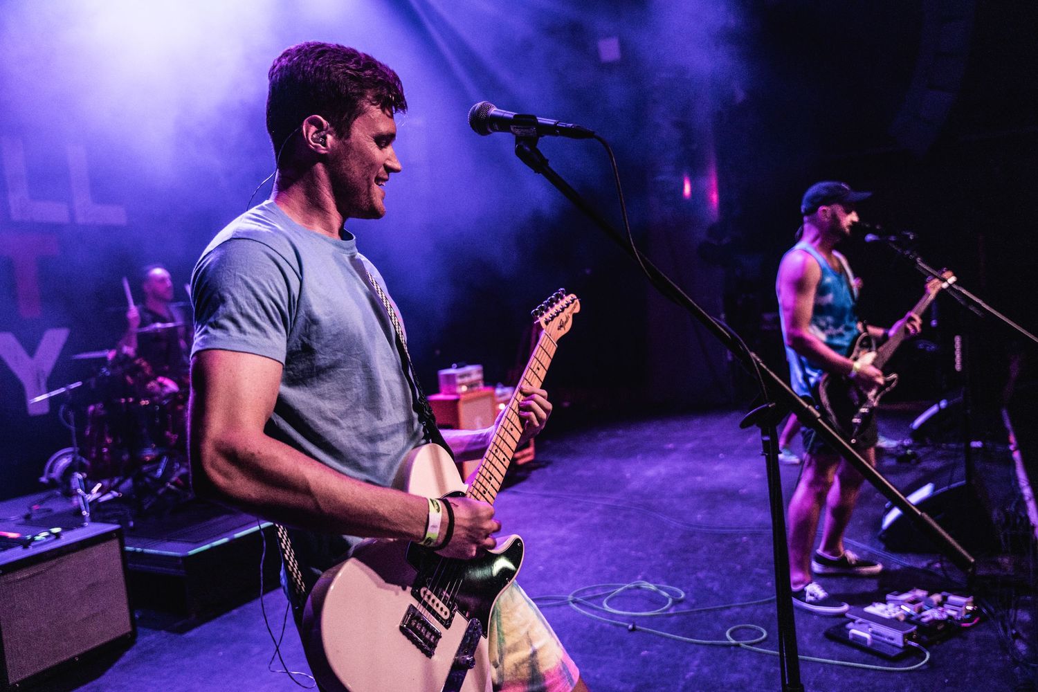 Musicians perform on stage with electric guitars under dramatic purple lighting at a rock concert.