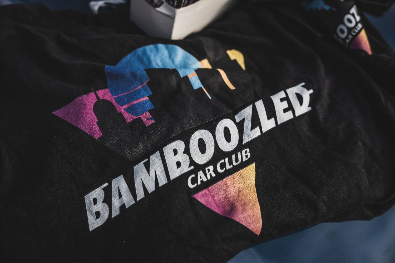 Black t-shirt with Bamboozled Car Club logo design featuring colorful geometric patterns.