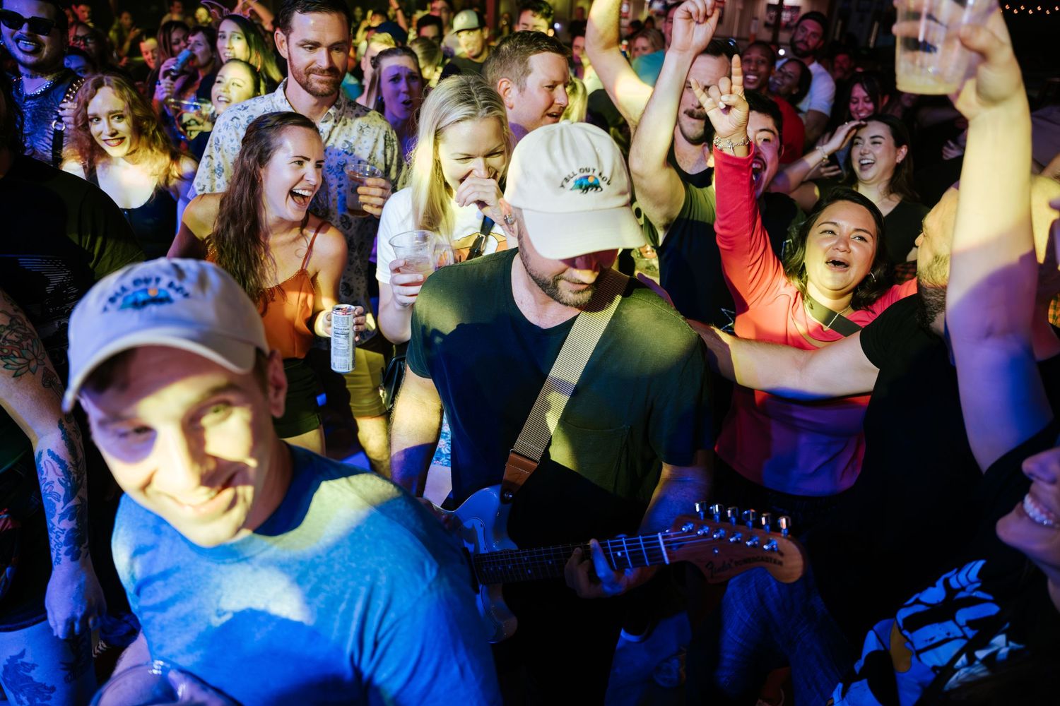 Concert attendees dance and celebrate while musician plays guitar in a crowded venue.