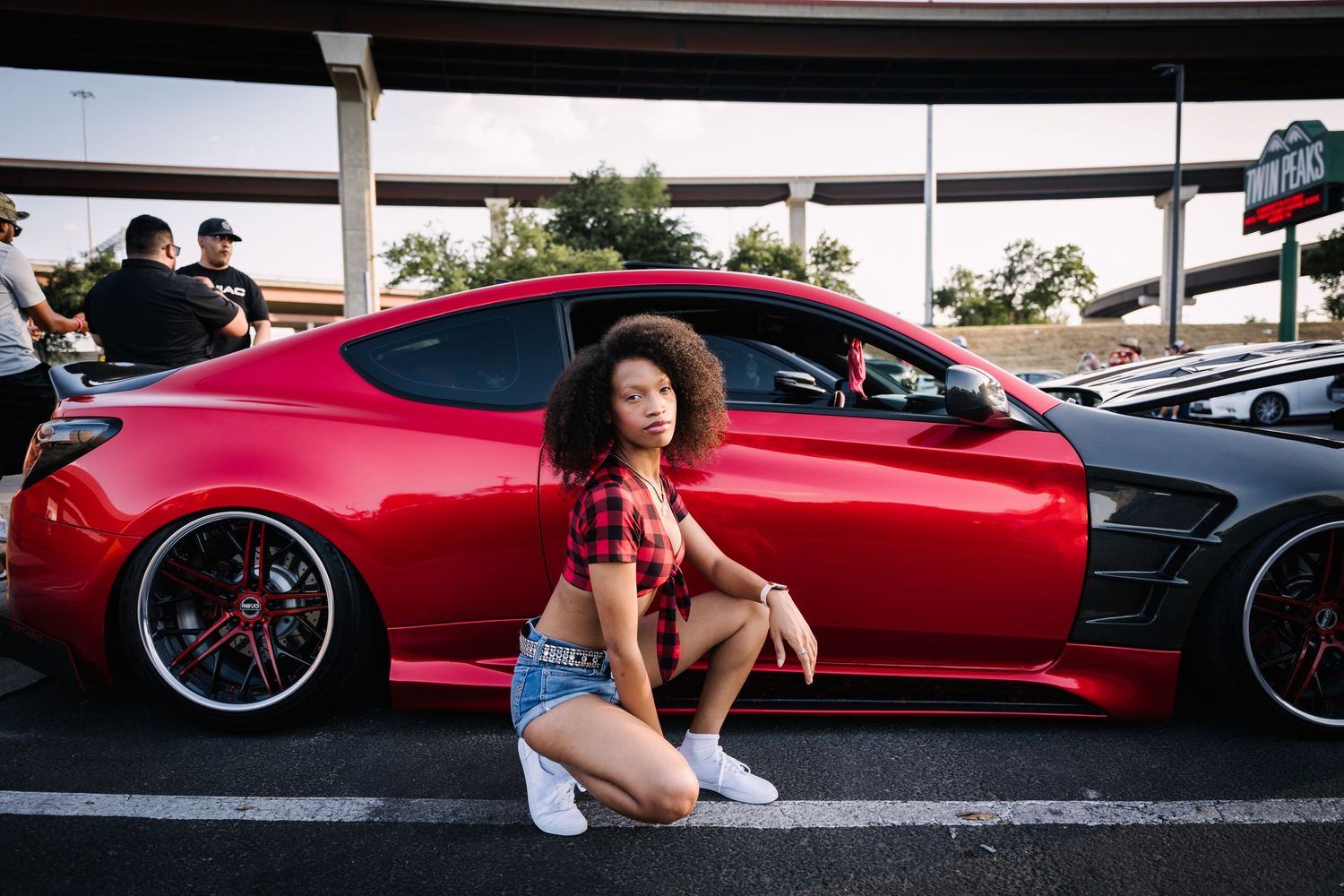 Red sports car with custom wheels parked at an outdoor car meet.