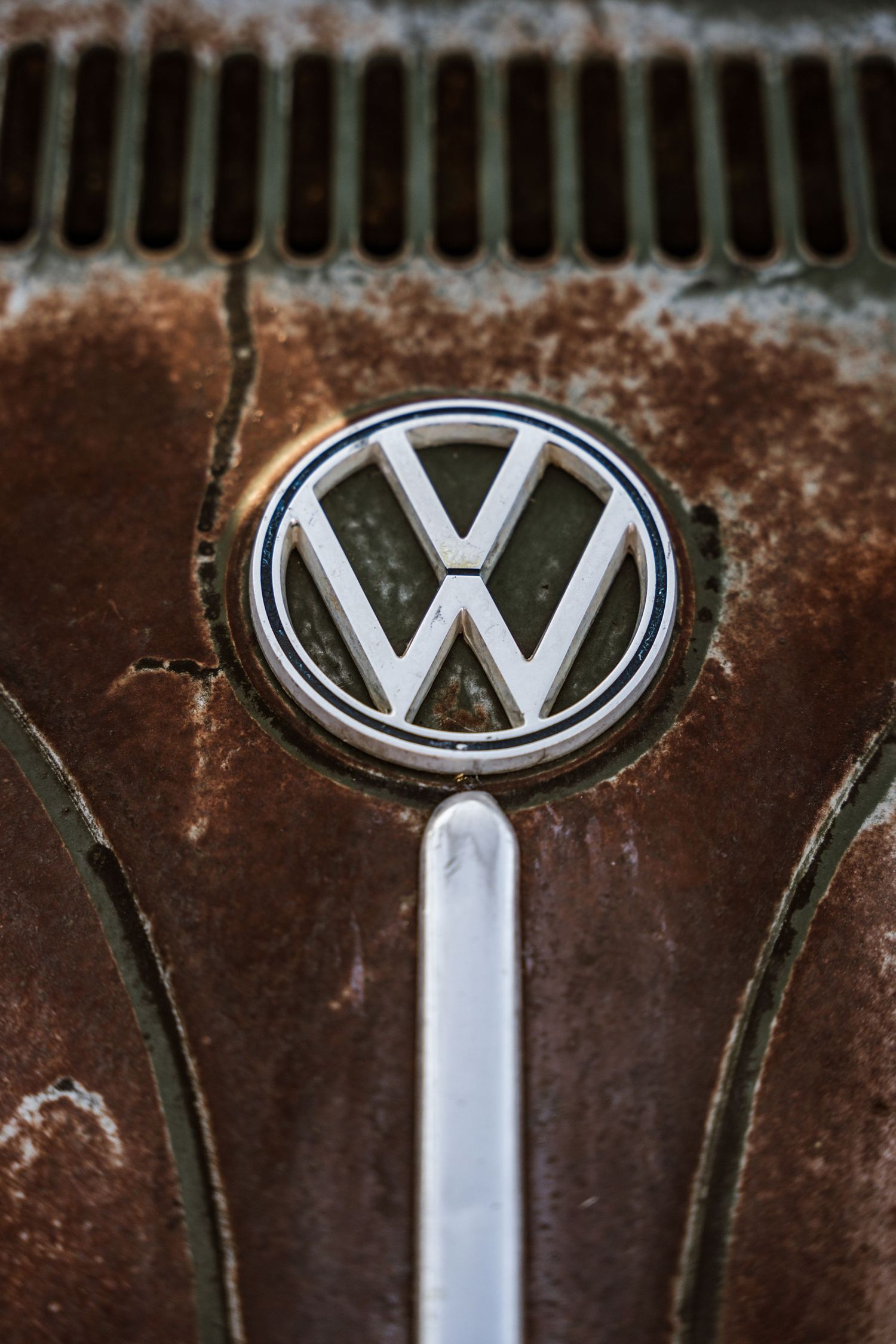 Close-up of a rusty vintage Volkswagen logo badge on weathered metal.