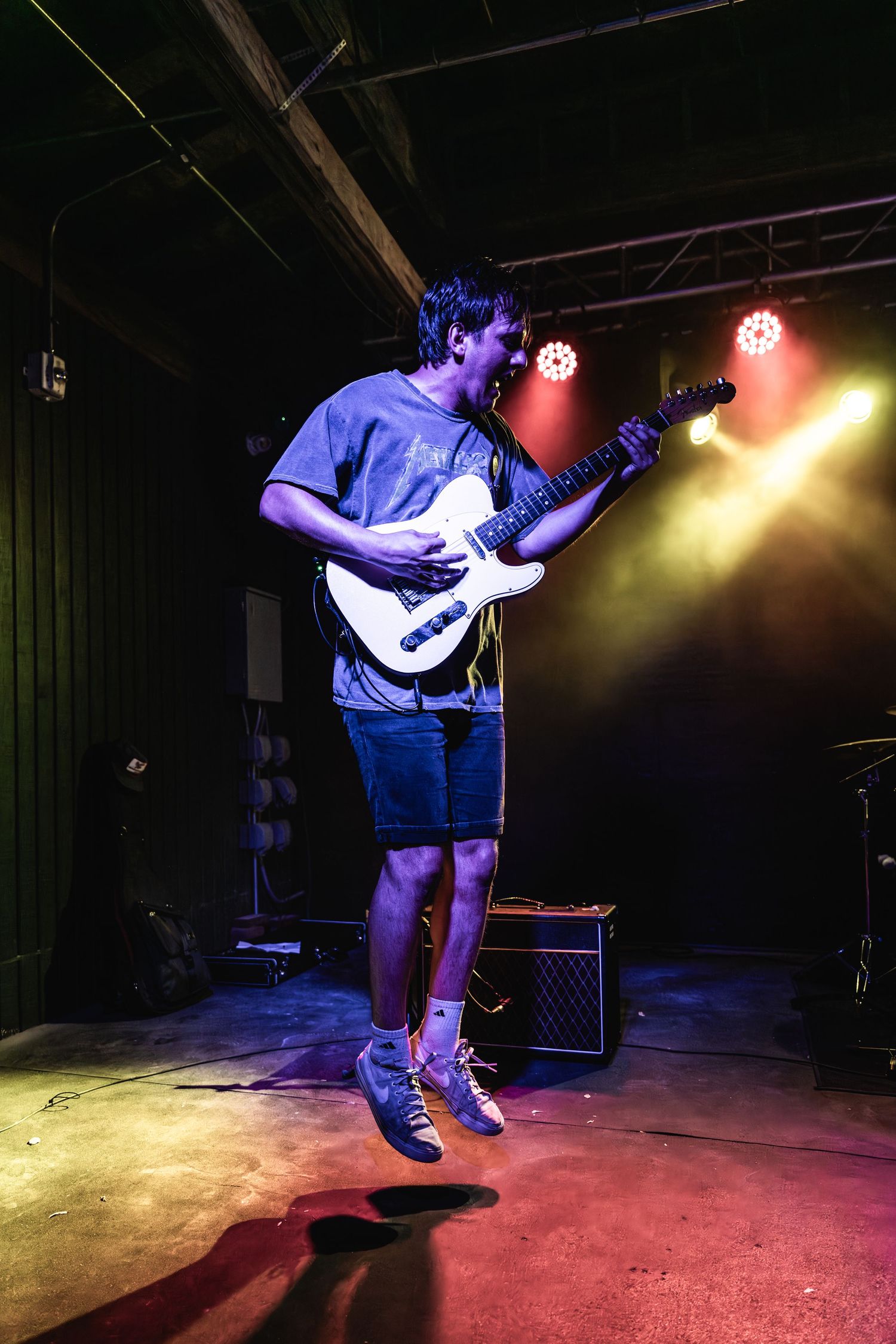 Guitarist jumps while playing under colorful stage lights during energetic performance.