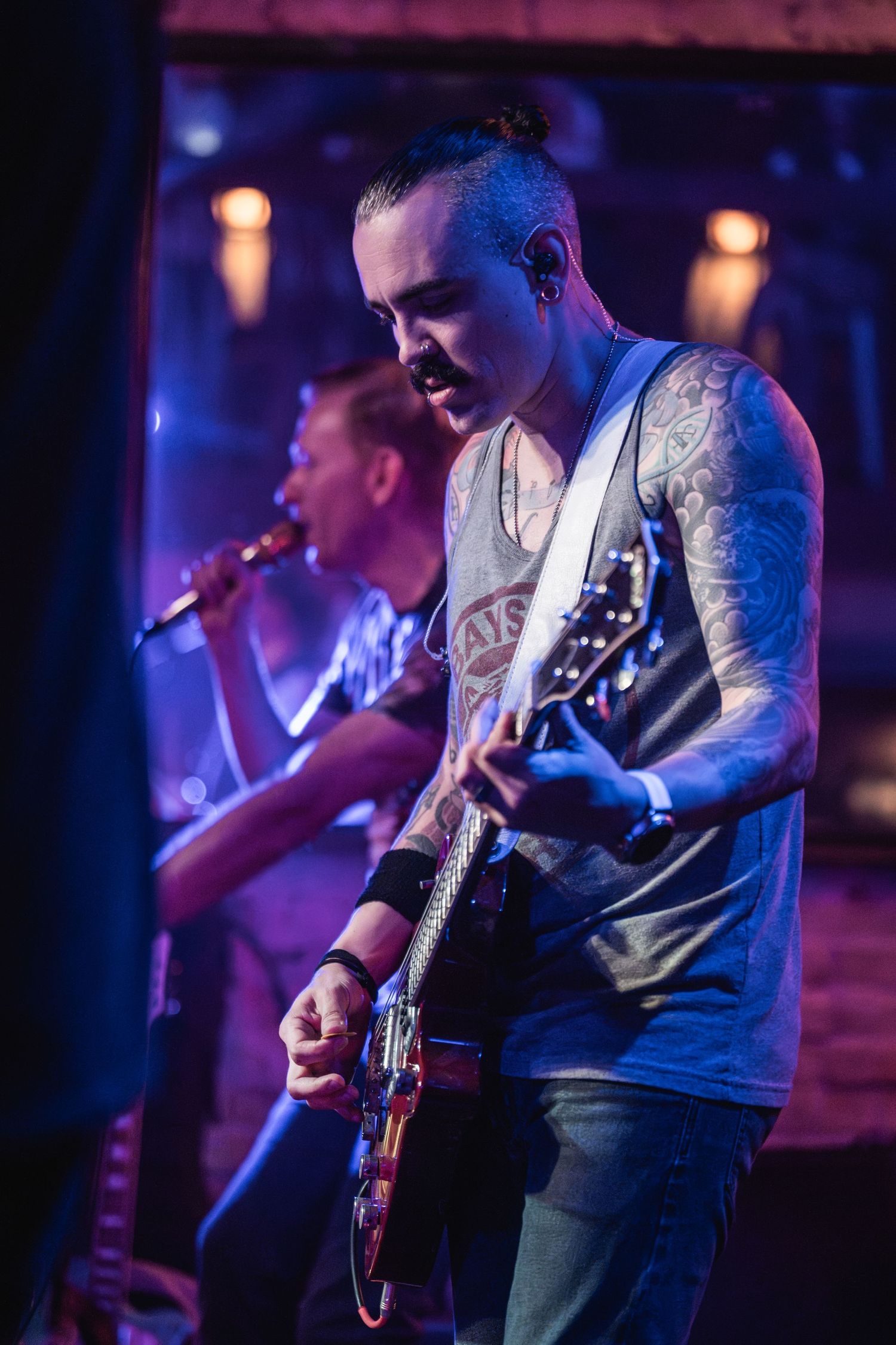 A musician with tattoos plays electric guitar under blue stage lighting during a performance.