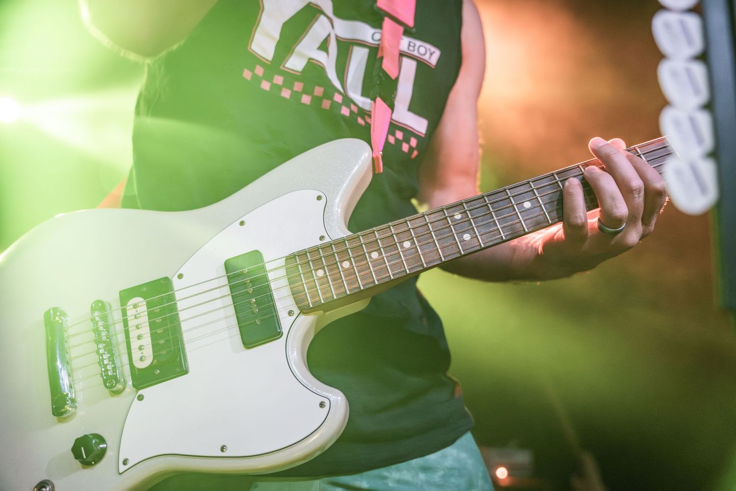 Close up shot of hands playing a white electric guitar with green lighting.