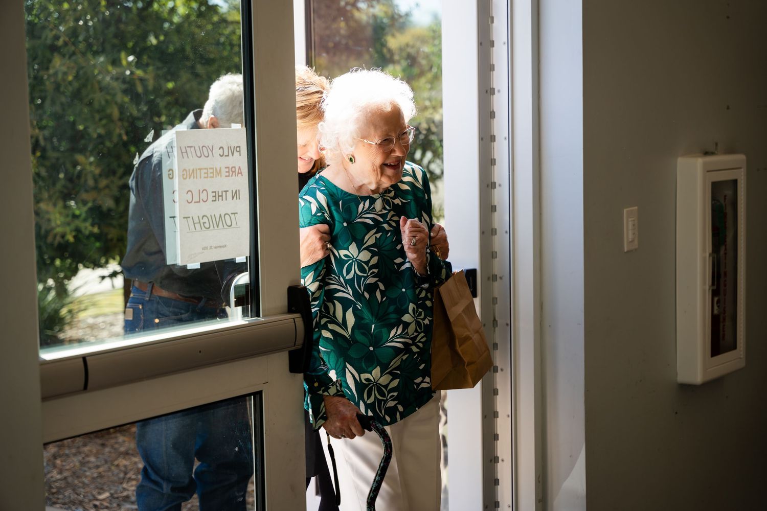 A person in a green floral dress entering through a glass door.