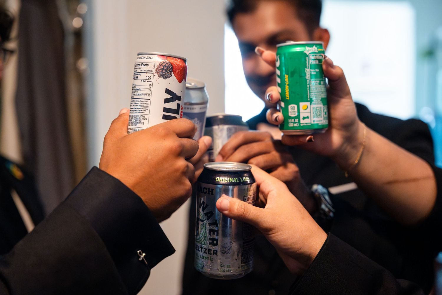 Wedding party members toast with various canned beverages during preparation.