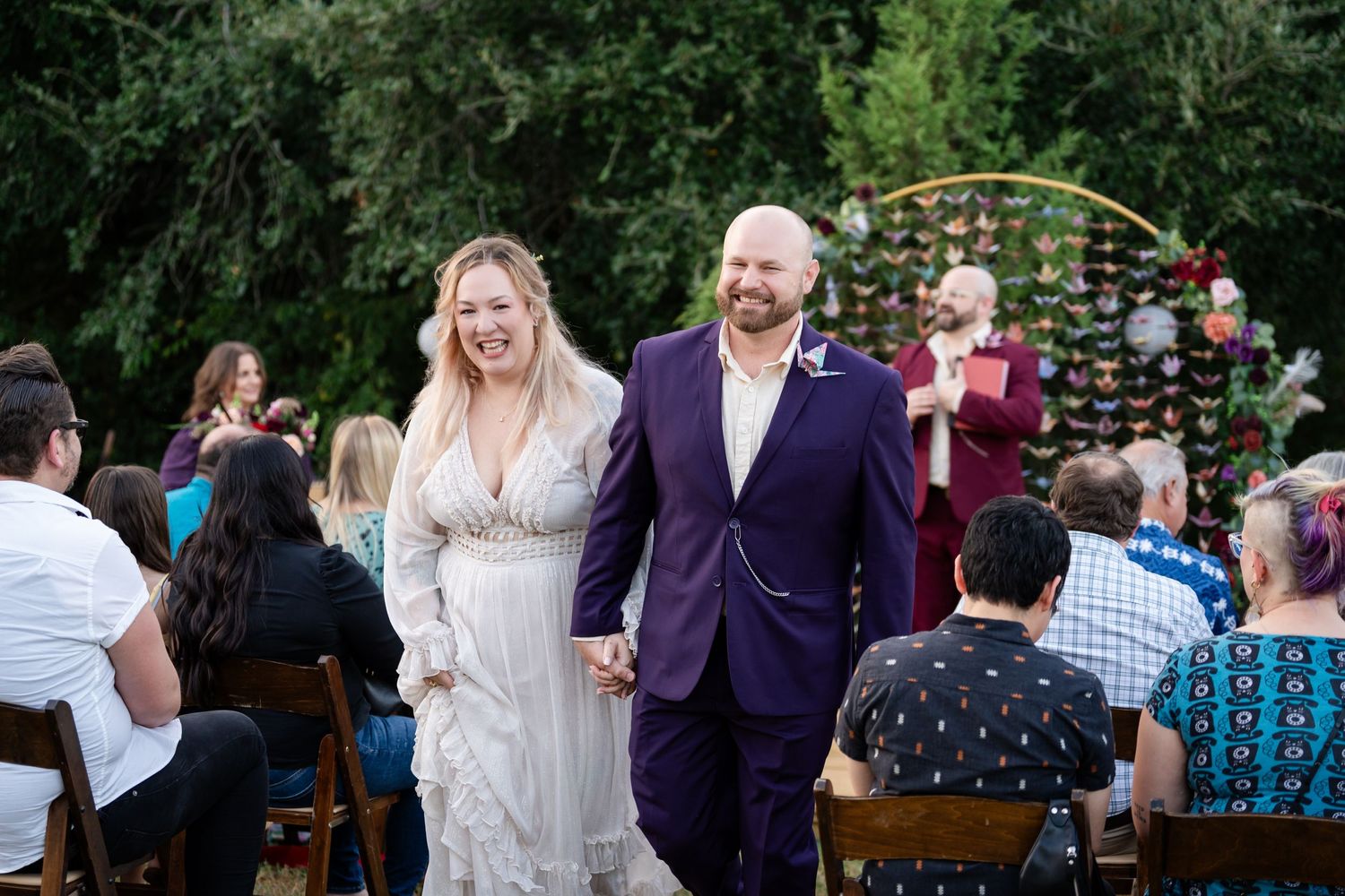 Newlyweds walk down the aisle past seated guests under a decorated arch with paper butterflies.