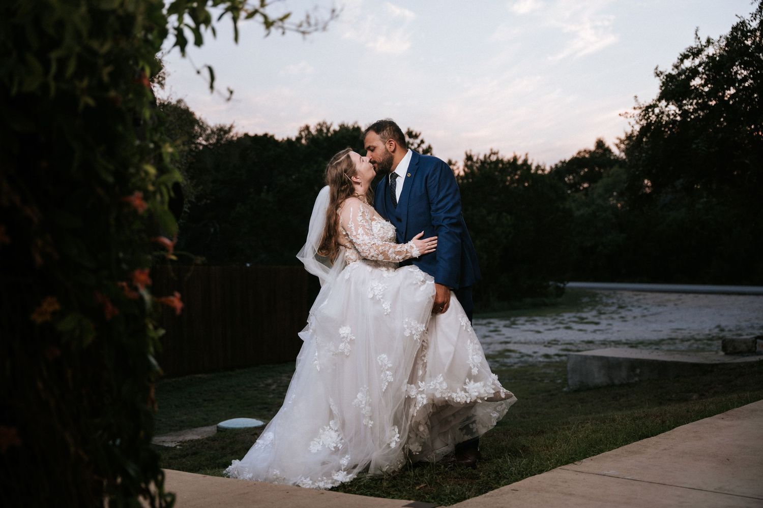 A romantic sunset portrait of a couple in wedding attire by a lake with trees in the background.