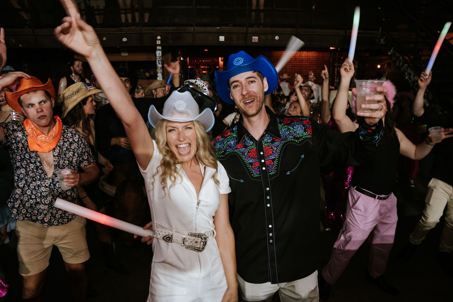 Party crowd holding light-up sticks and dancing at a nighttime event.