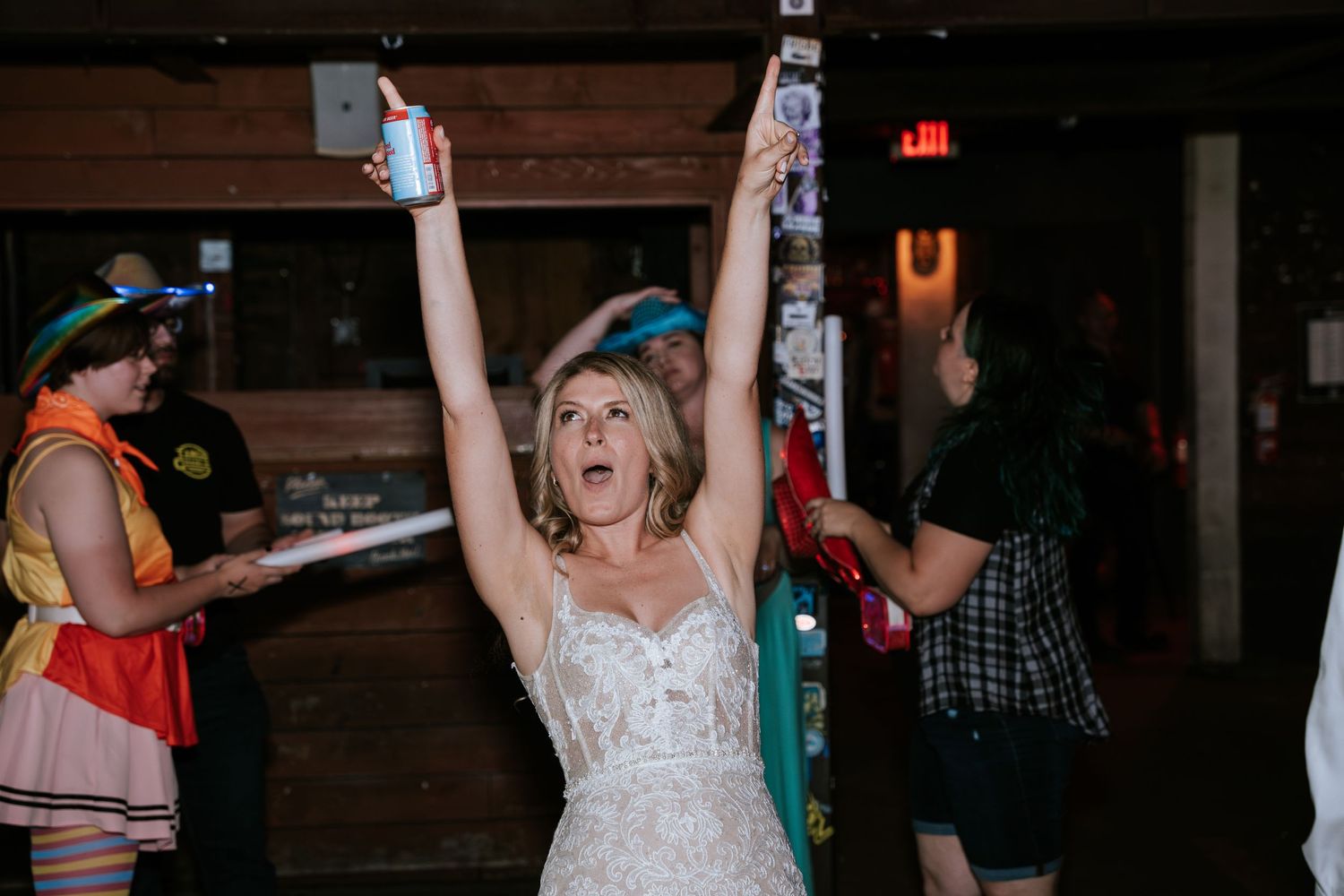 A bride in a white lace dress celebrates enthusiastically on the dance floor at a wedding reception.