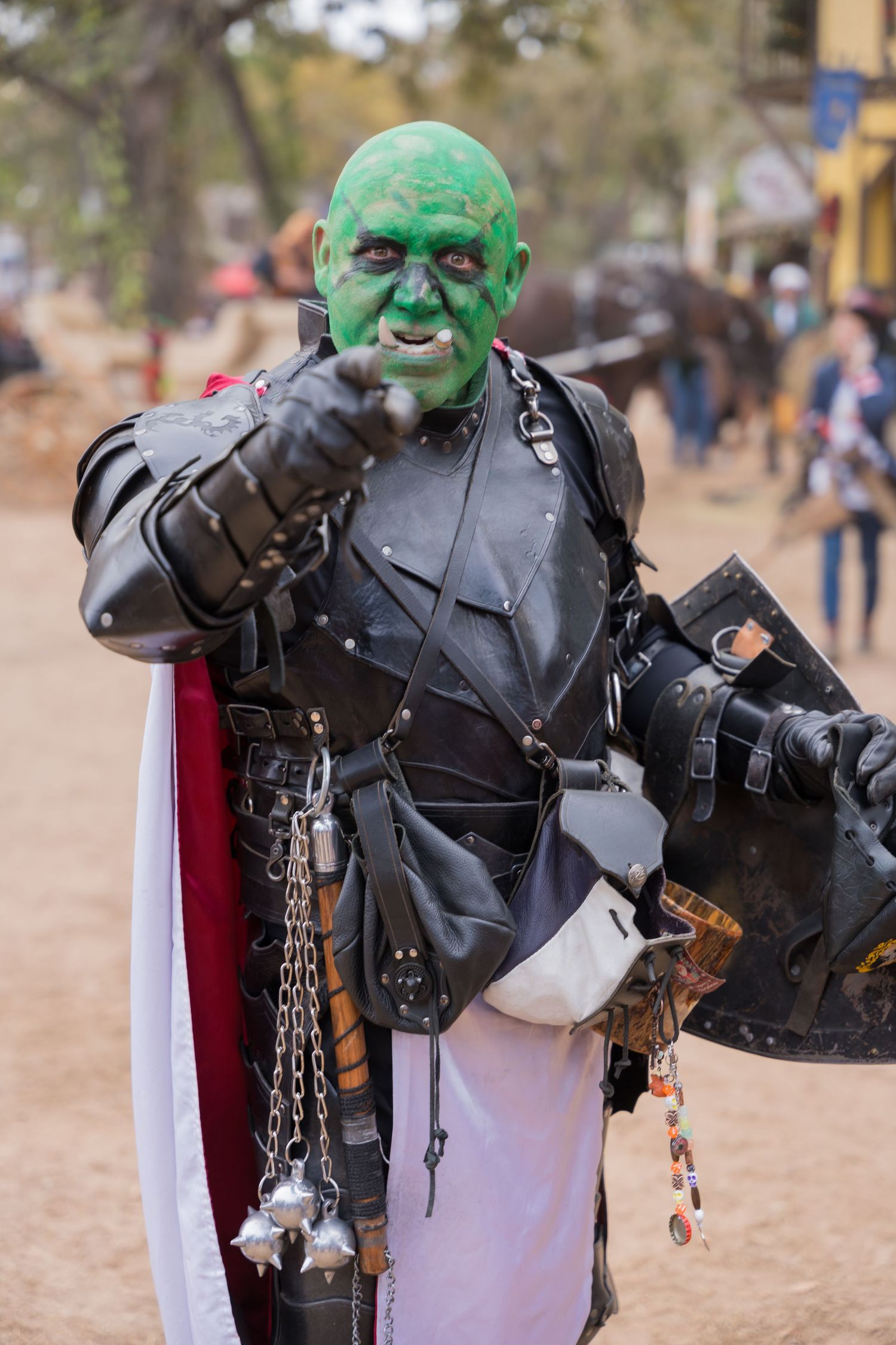 Costumed character with green face paint and leather armor poses menacingly at a renaissance festival.