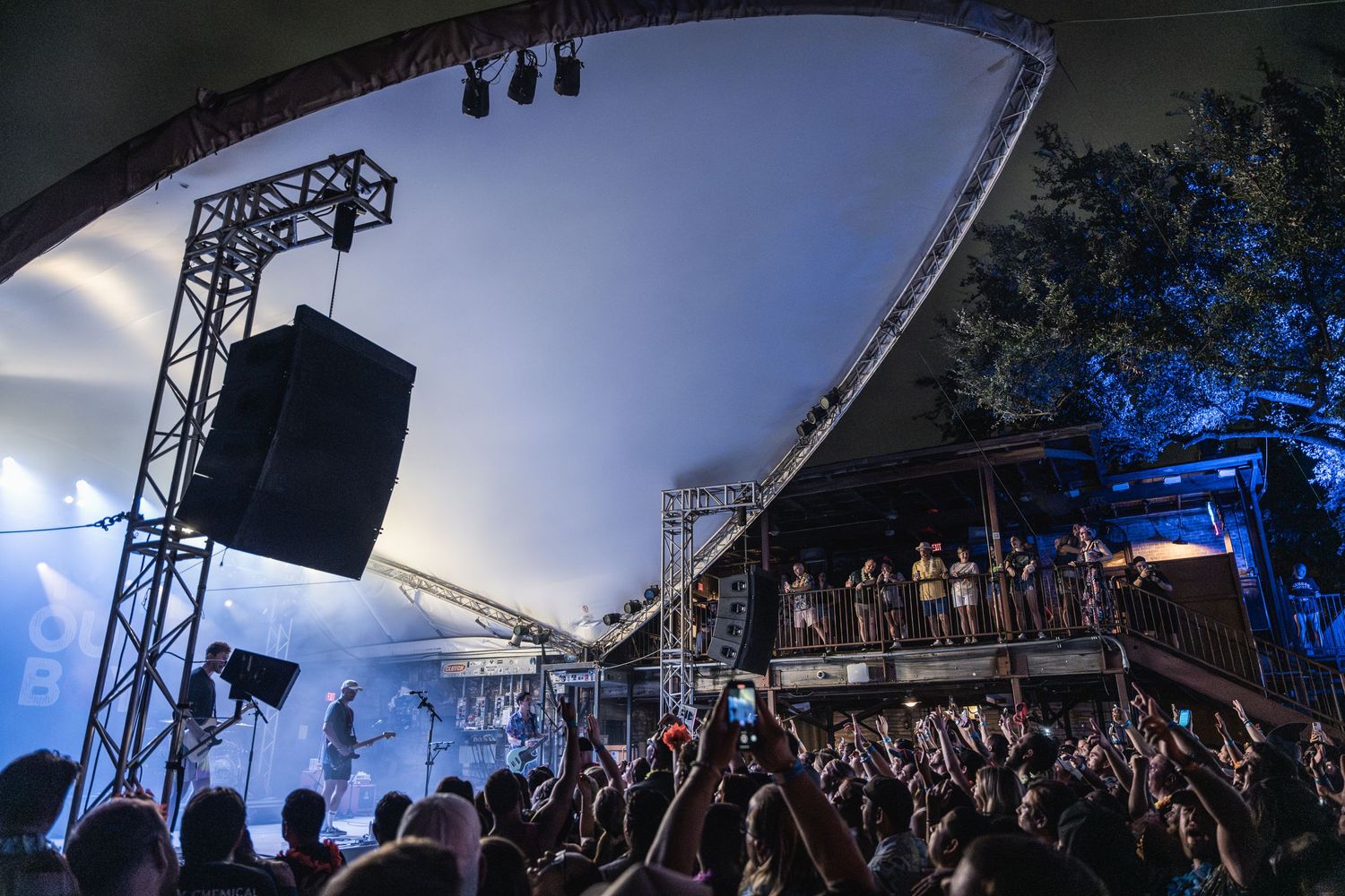 Concert venue with curved tent structure and stage lighting against evening sky.